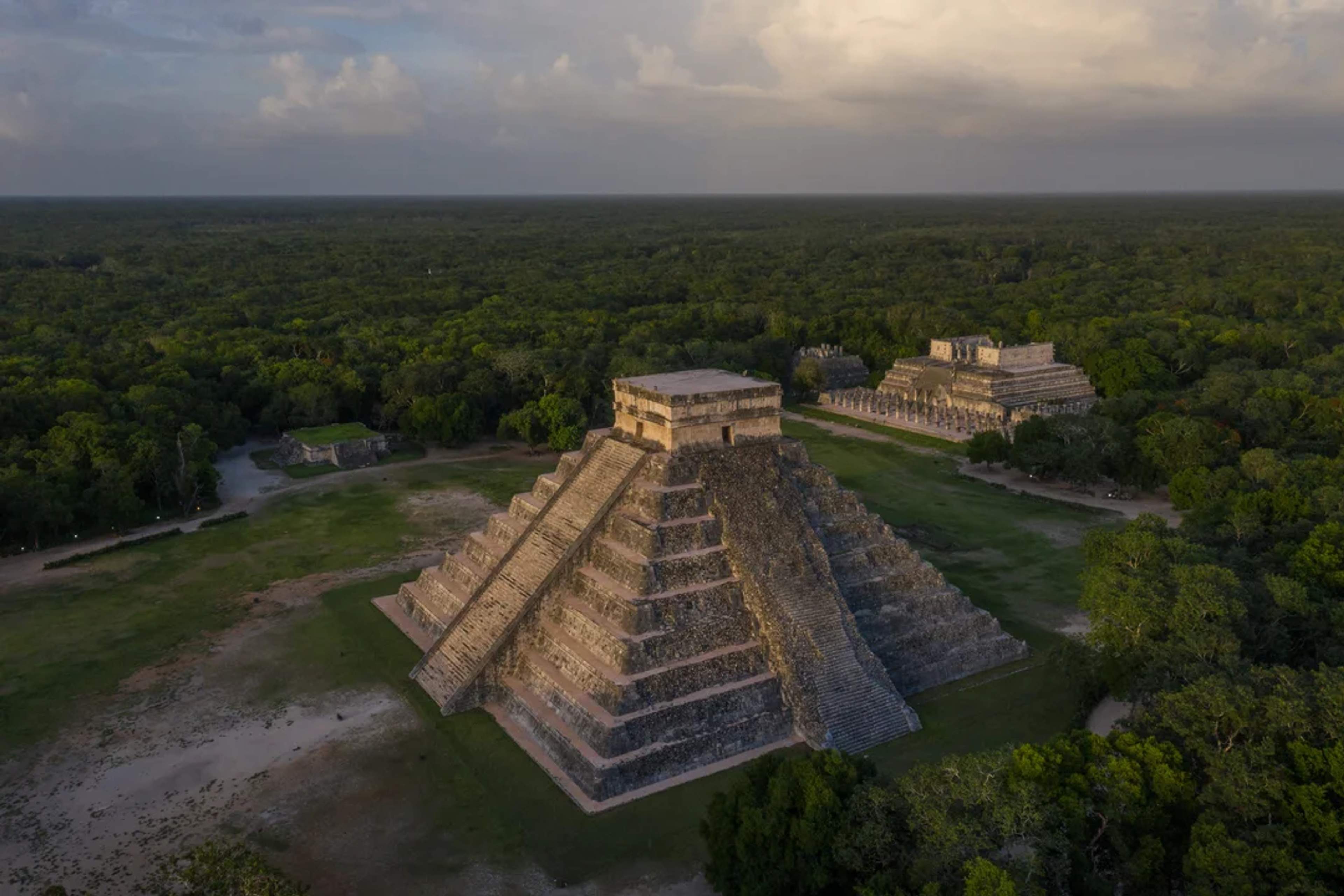 Aerial view of Chichén Itzá at sunset, surrounded by jungle and ancient Mayan structures.