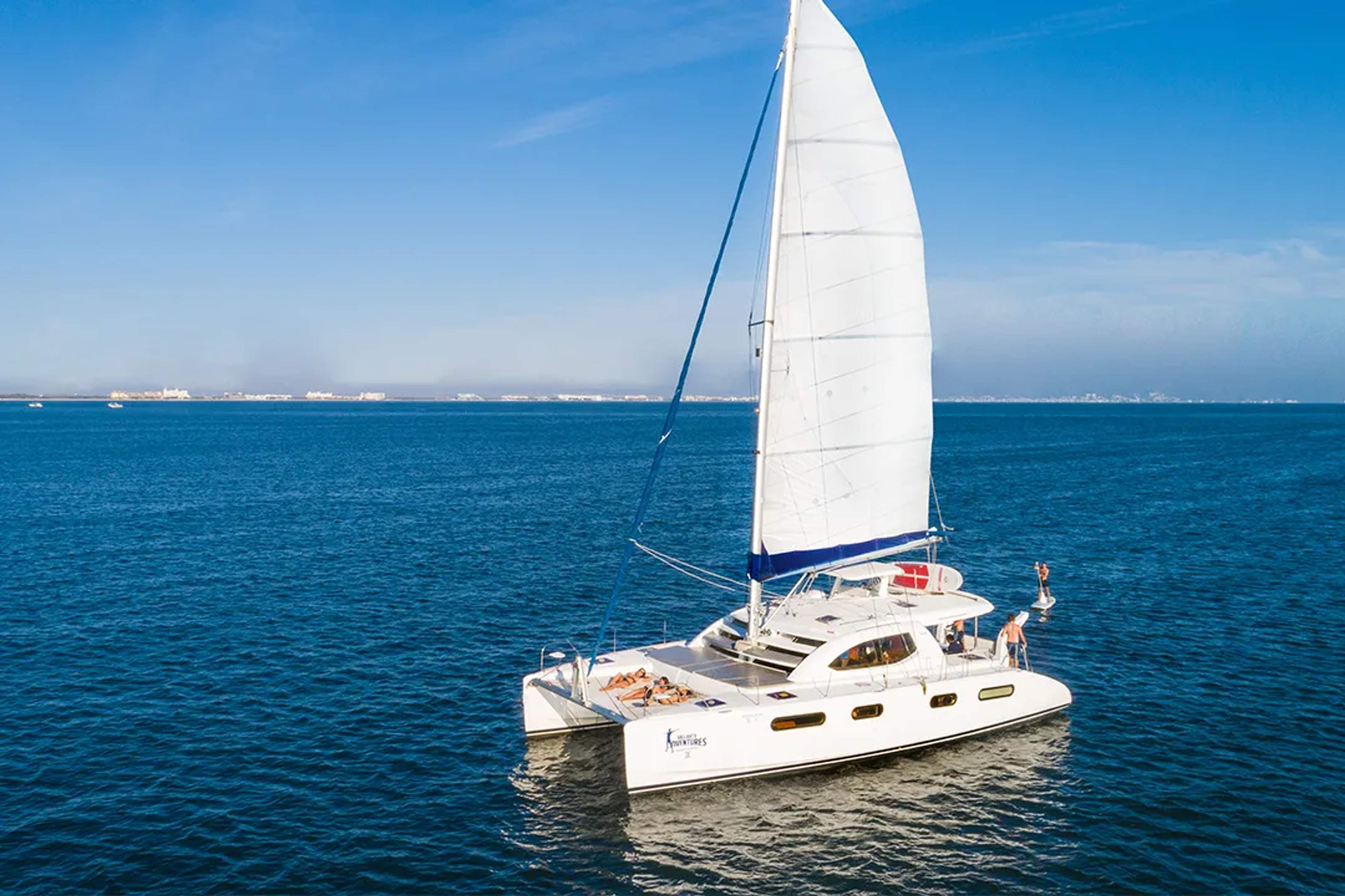 Catamarán de lujo navegando en aguas azules con personas relajándose y saltando al mar.