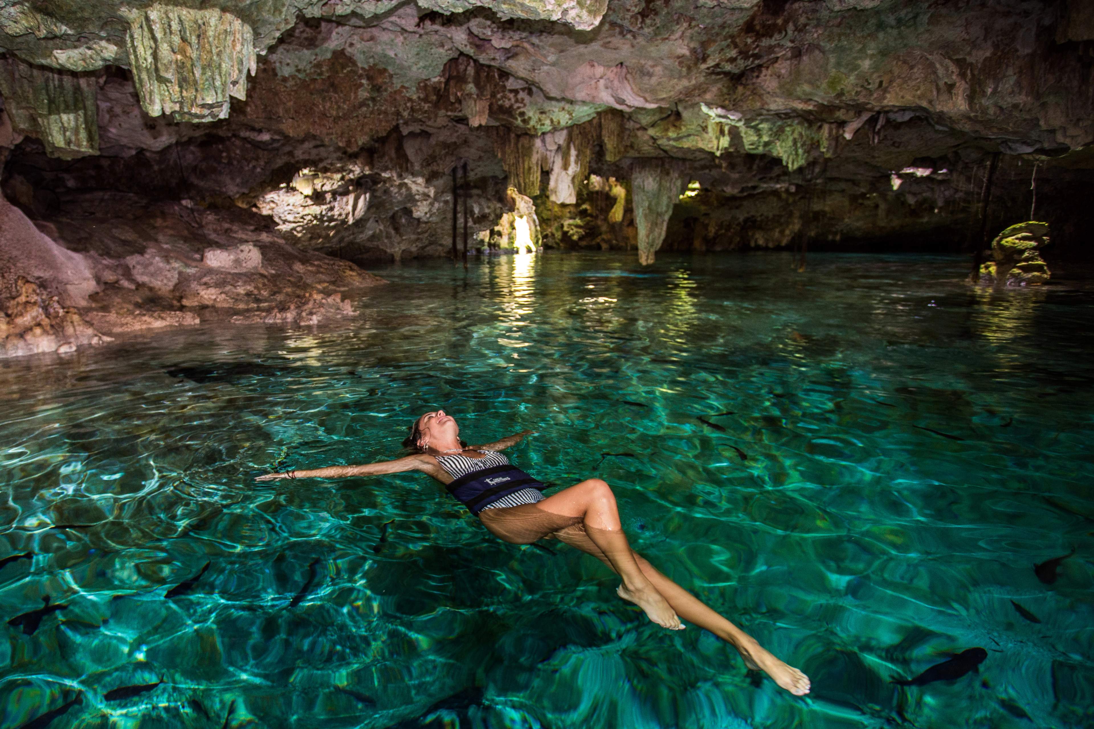 Person floating in clear turquoise water inside a cave, surrounded by rock formations.