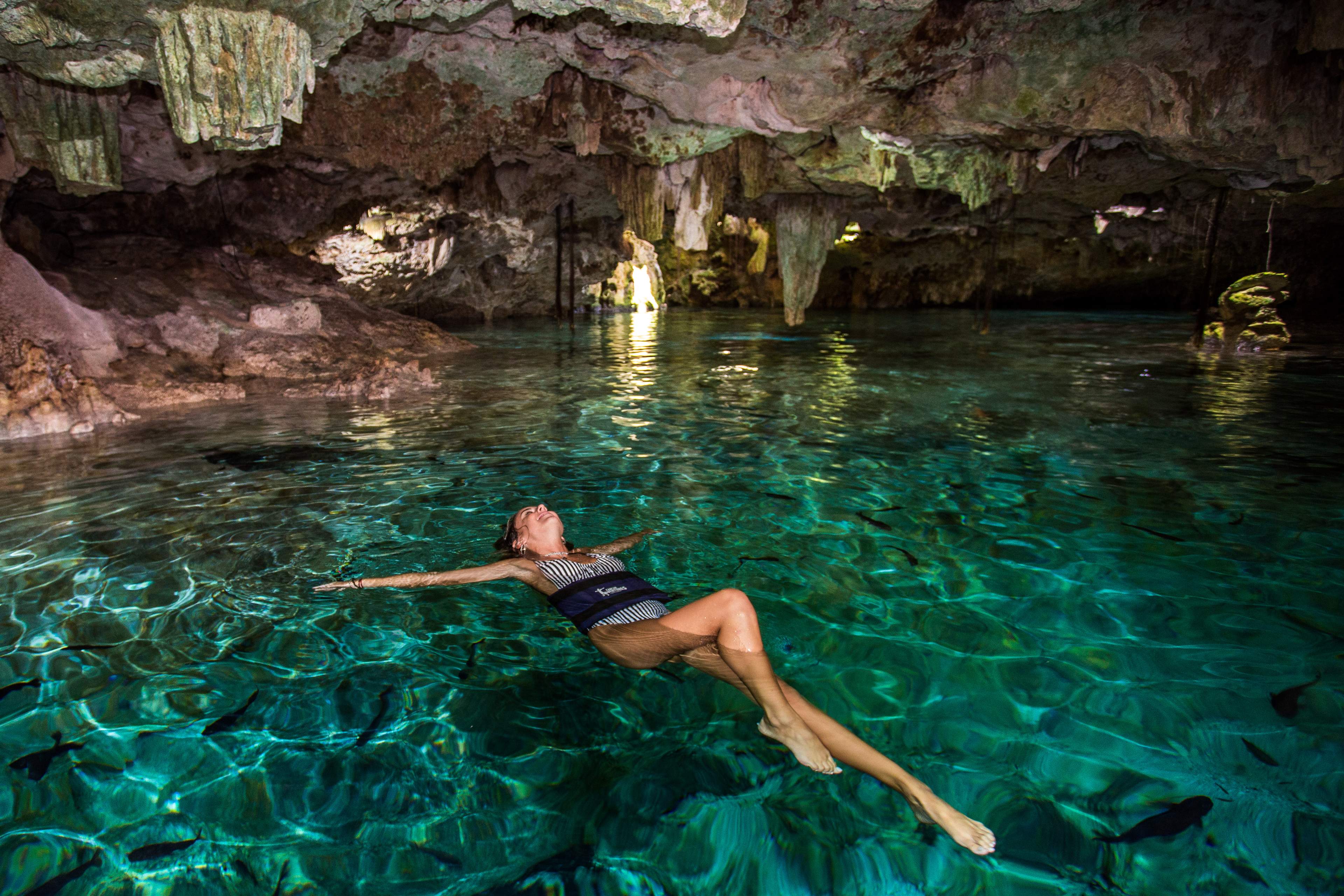 Person floating in clear turquoise water inside a cave, surrounded by rock formations.