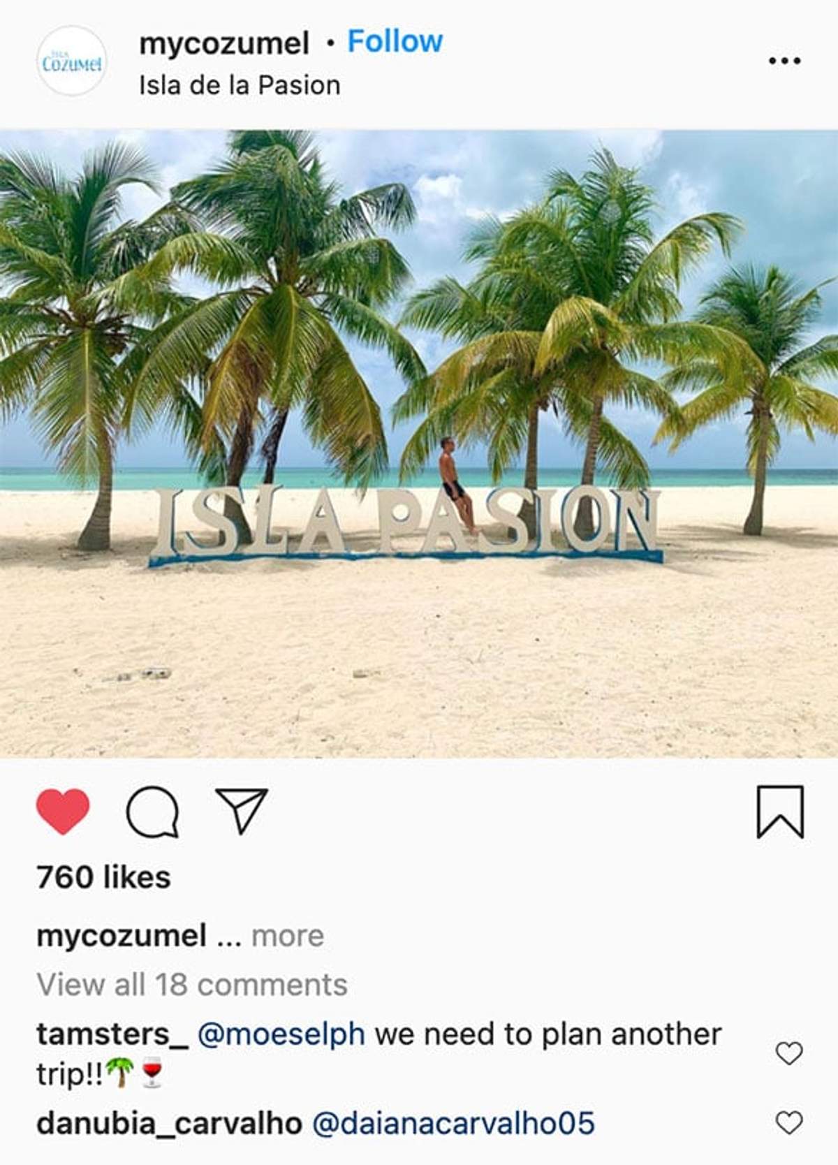 A man standing by the "Isla Pasion" sign on a sandy beach in Cozumel, surrounded by palm trees and turquoise waters.