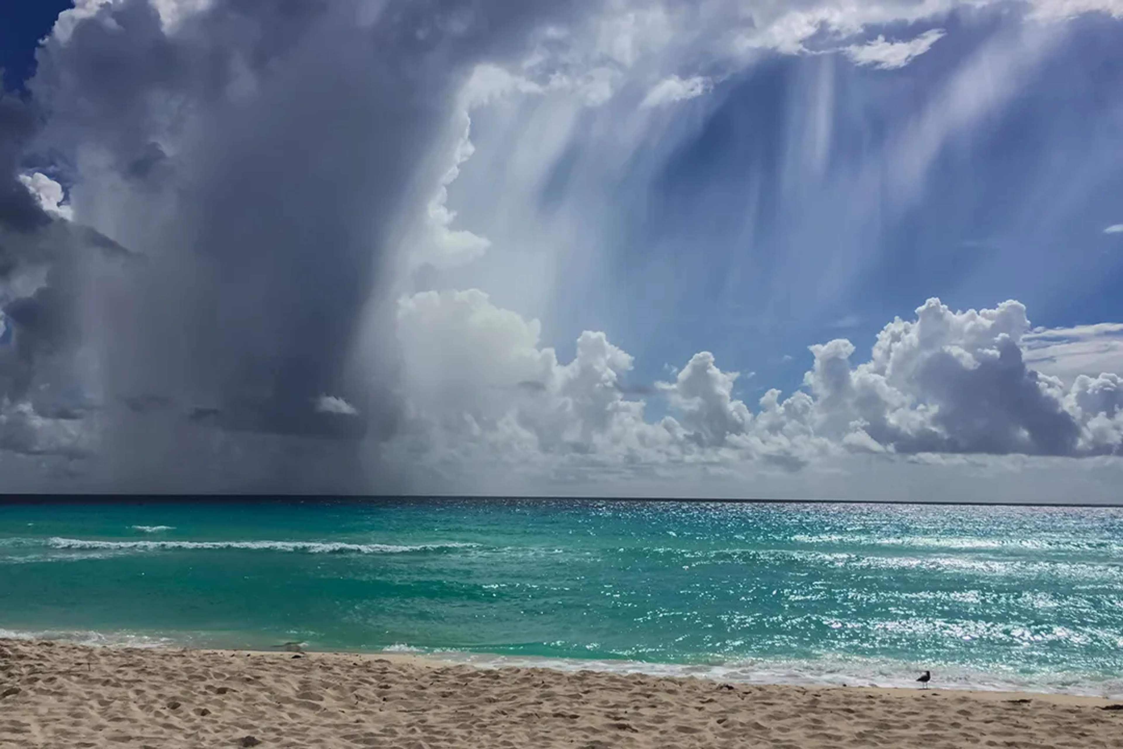 Mar Caribe en Cancun con agua turquesa, nubes de lluvia, olas iluminadas y playa de arena en Mexico