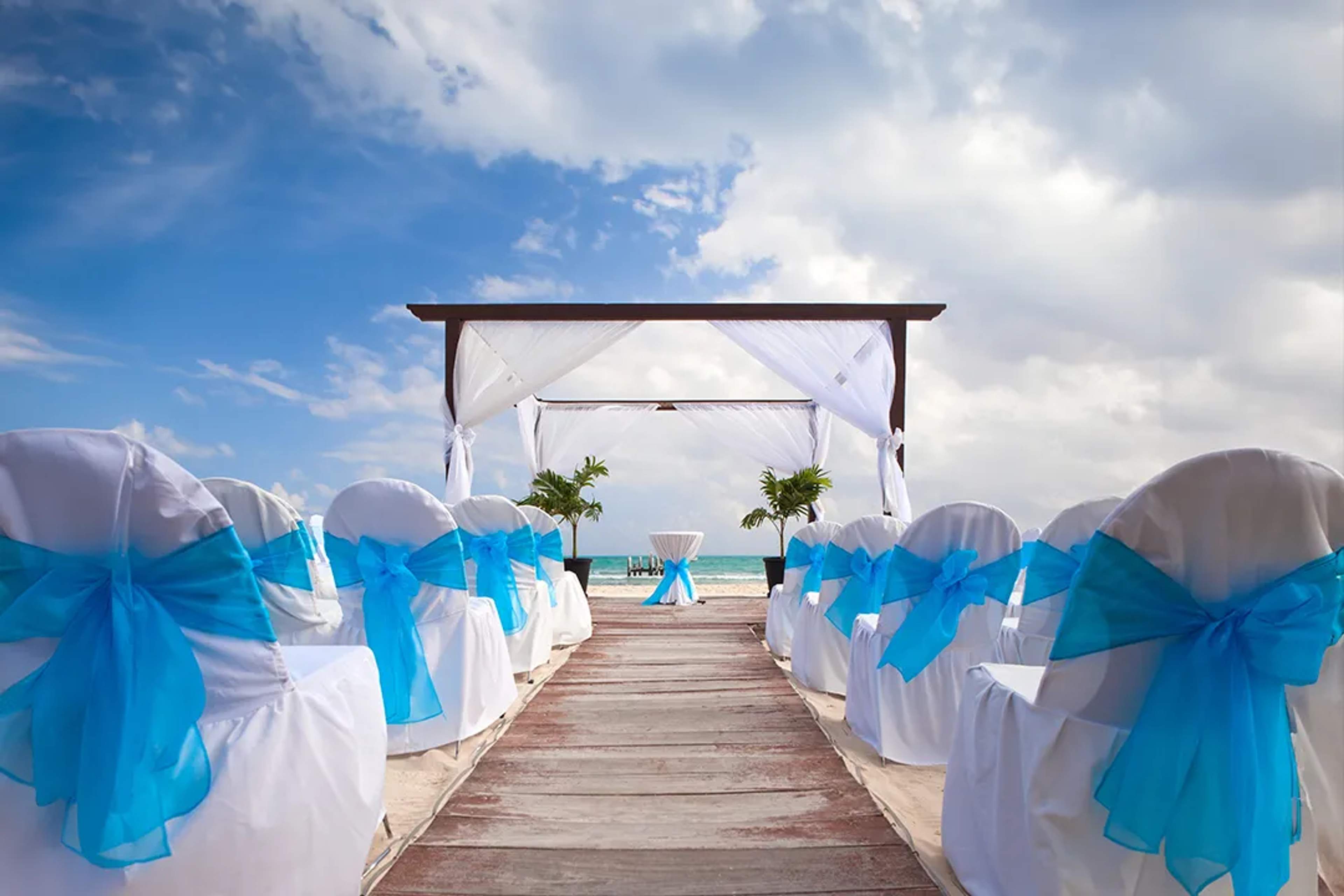 Arreglo de boda en la playa en Cancún con sillas blancas y lazos azules, ideal para bodas destino.