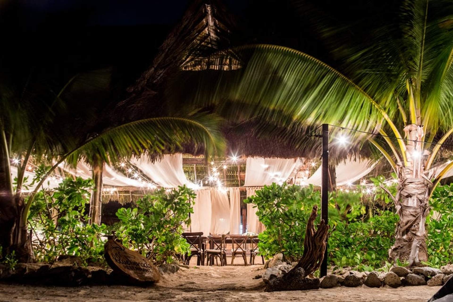 Montaje de boda bellamente iluminado por la noche en Punta Venado, Cancún, con decoración elegante y ambiente tropical.