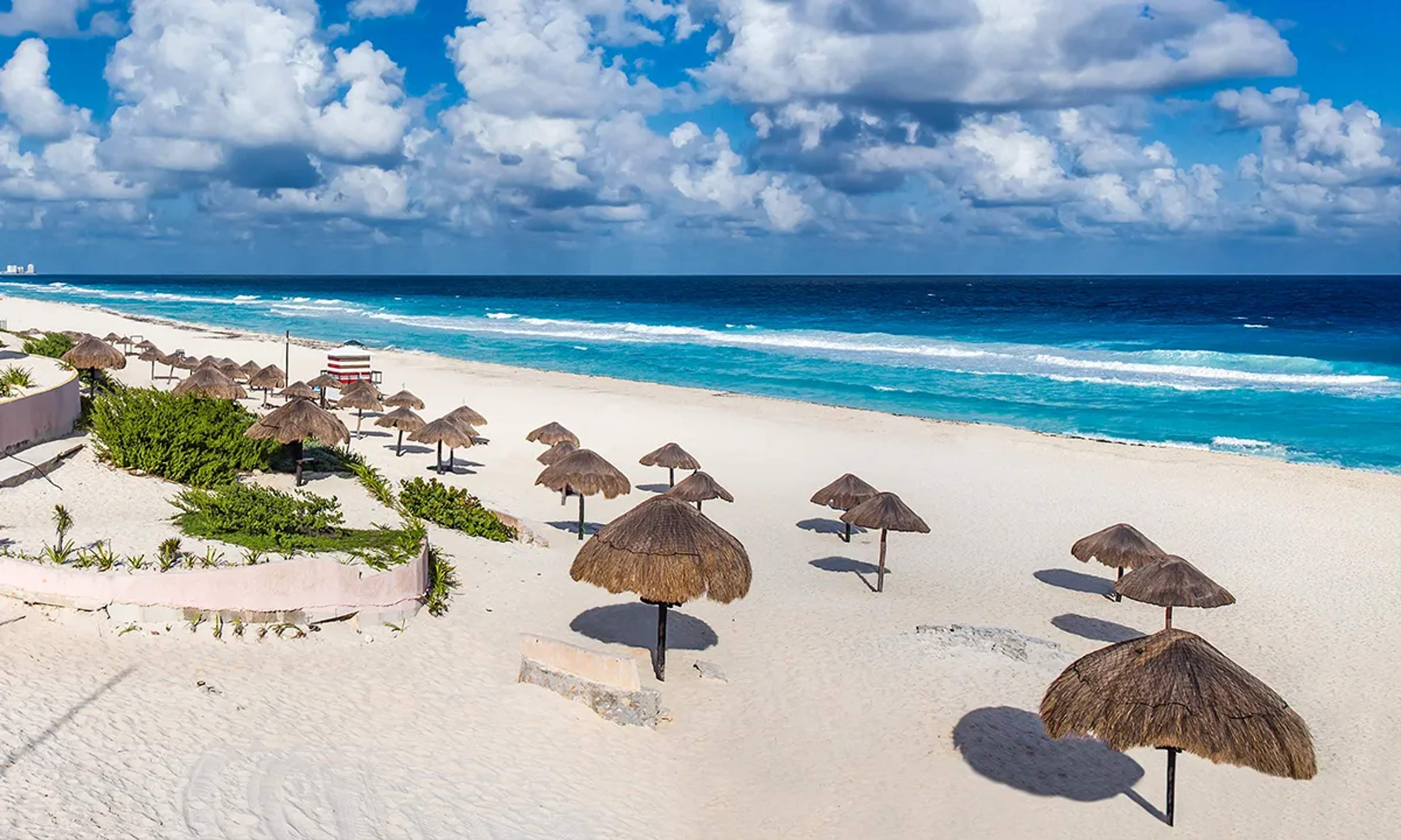 Playa Delfines in Cancun features white sands, turquoise waters, palapas for shade, and stunning views from its iconic lookout.