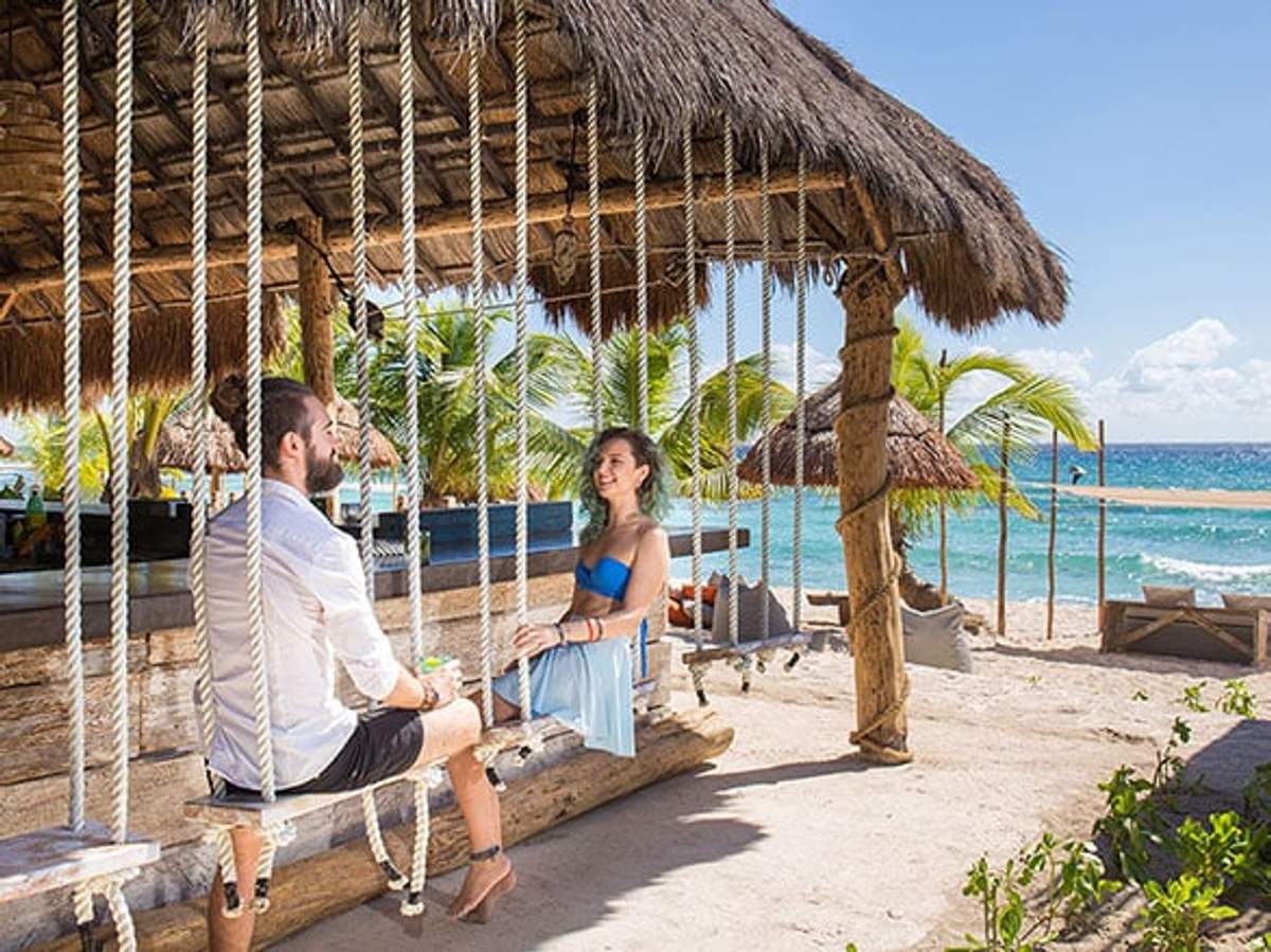 Pareja disfrutando de columpios en un bar de playa en Playa del Carmen con una hermosa vista al mar.