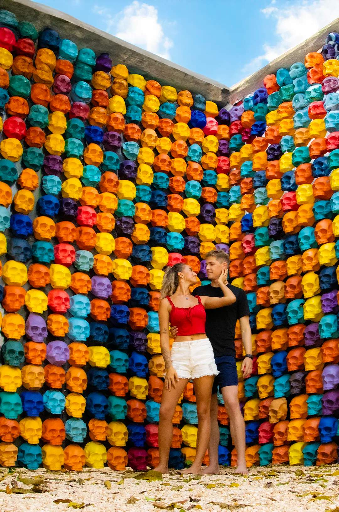 Couple posing in front of a colorful skull wall in Tulum
