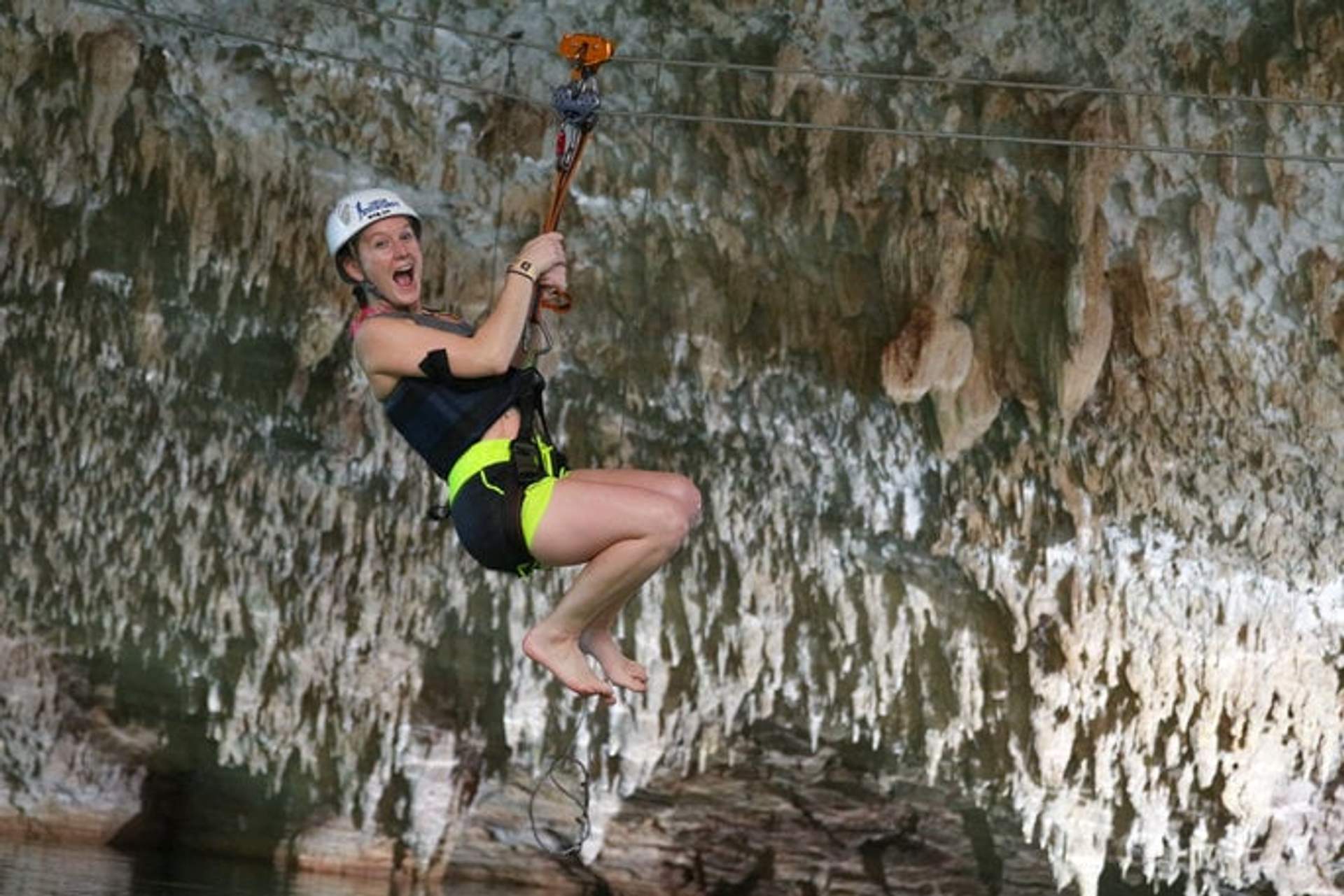 Una mujer haciendo tirolesa dentro de una cueva, con casco y arnés, y una expresión de emoción en su rostro.