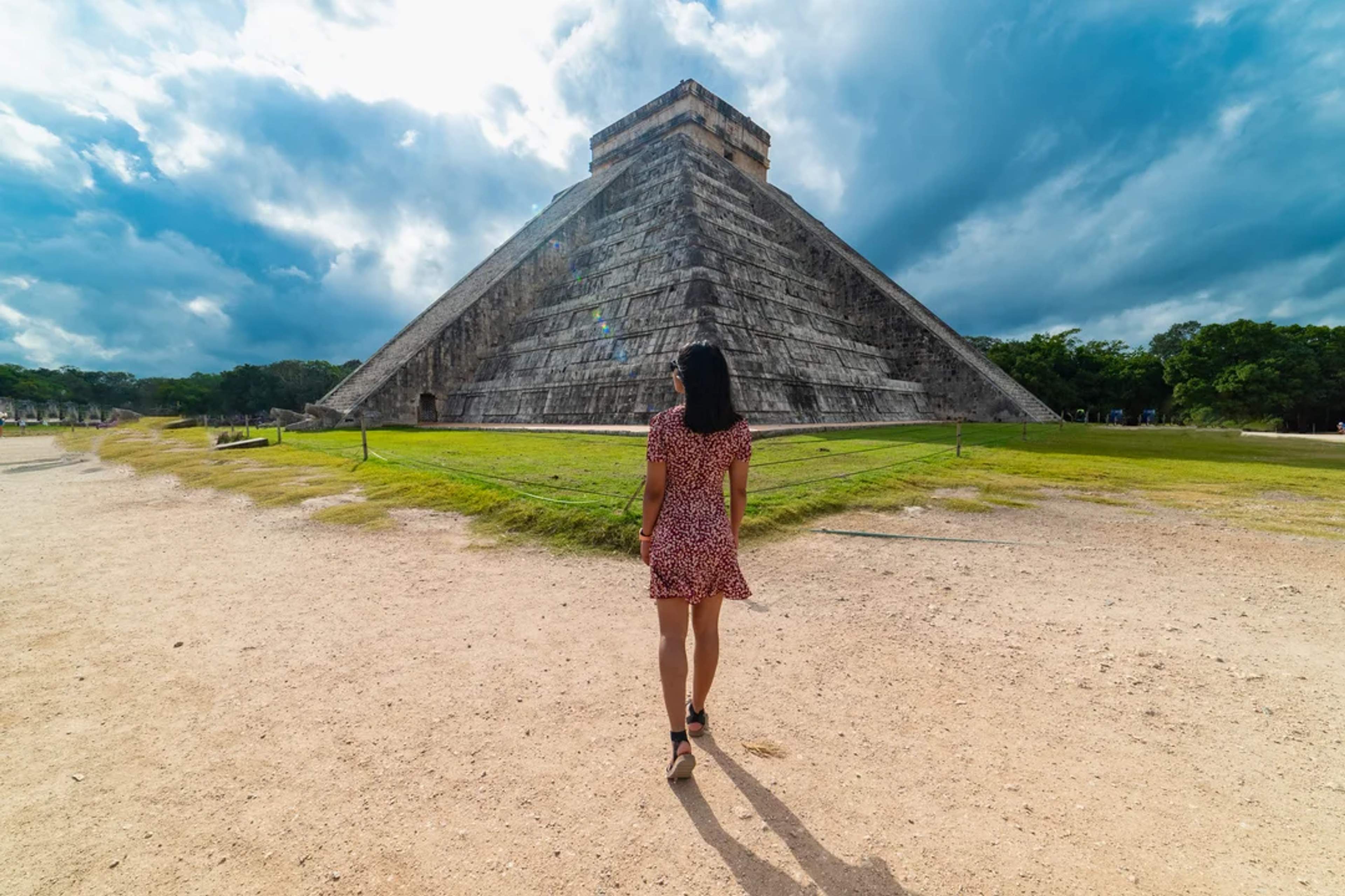 Mujer camina hacia el Templo de Kukulcán en Chichén Itzá bajo un cielo nublado y dramático.