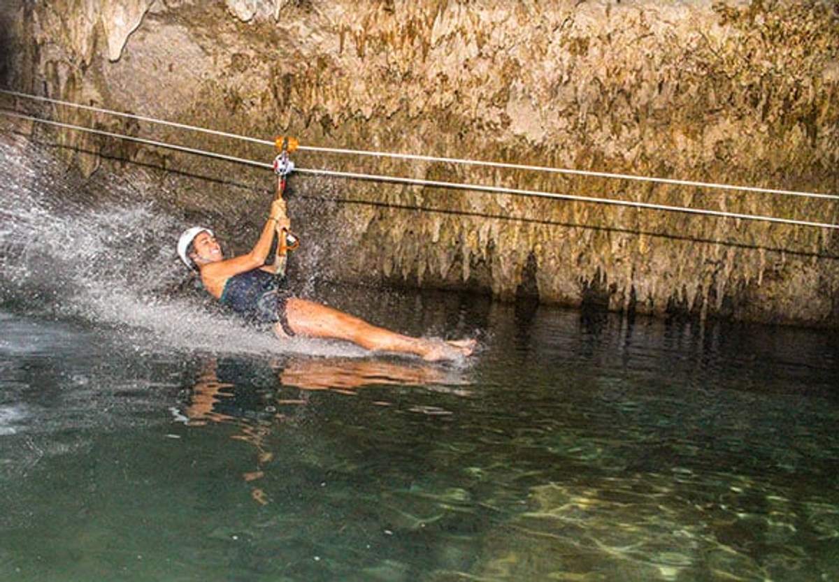 Una mujer deslizándose en tirolesa hacia el agua dentro de un cenote en Cancún, salpicando al entrar en contacto con el agua.