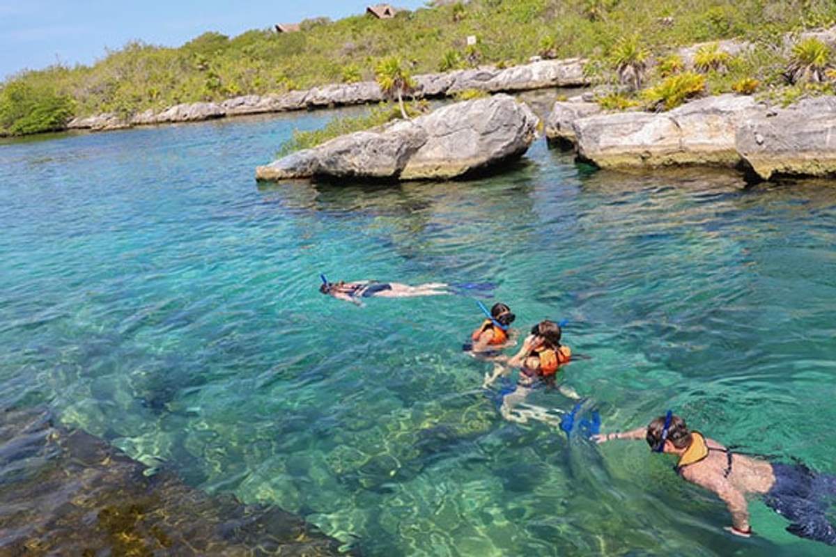 Personas haciendo snorkel en las aguas claras de la Laguna Yal Kú, rodeadas de formaciones rocosas.