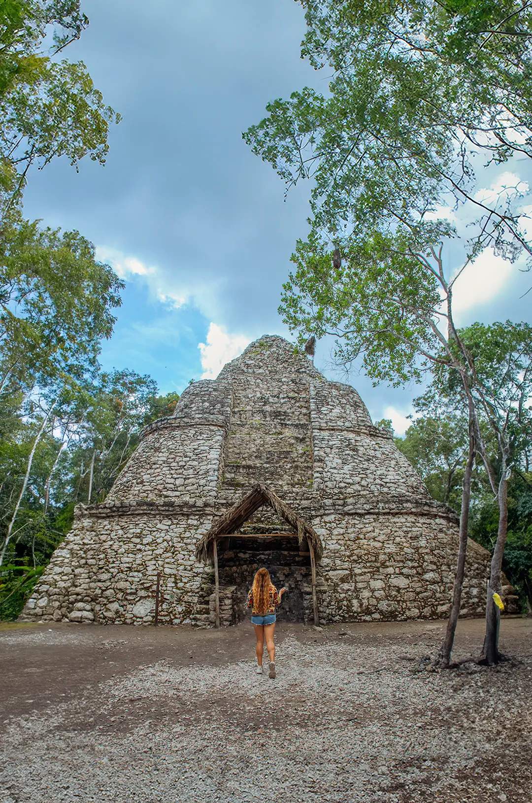 Woman walking towards an ancient Mayan stone structure in the middle of the jungle.