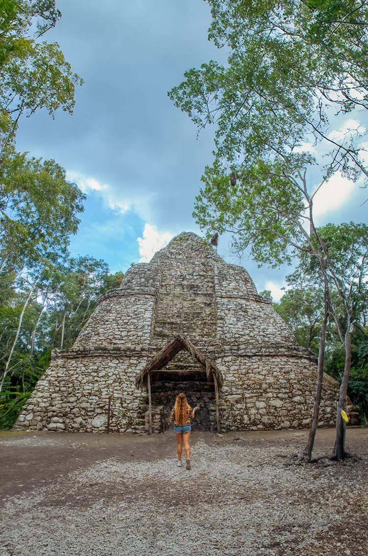 Woman walking towards an ancient Mayan stone structure in the middle of the jungle.