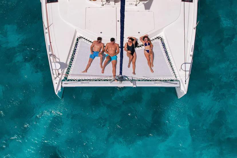 Elegante catamarán blanco navegando cerca de la costa bajo un cielo brillante y aguas turquesa.
