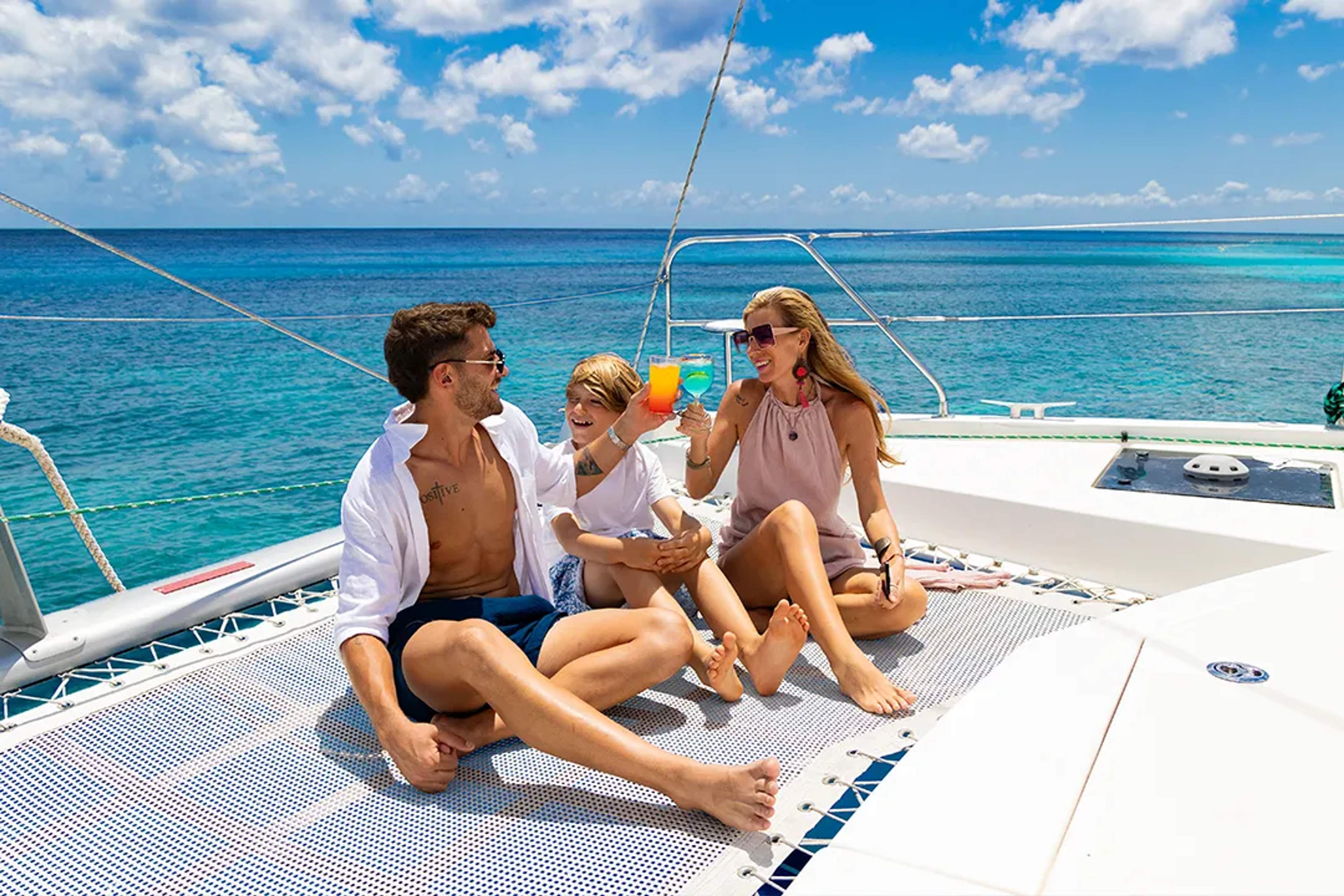 Family enjoying a catamaran sailing experience in the Caribbean Sea, relaxing with drinks and ocean views in Cancun.