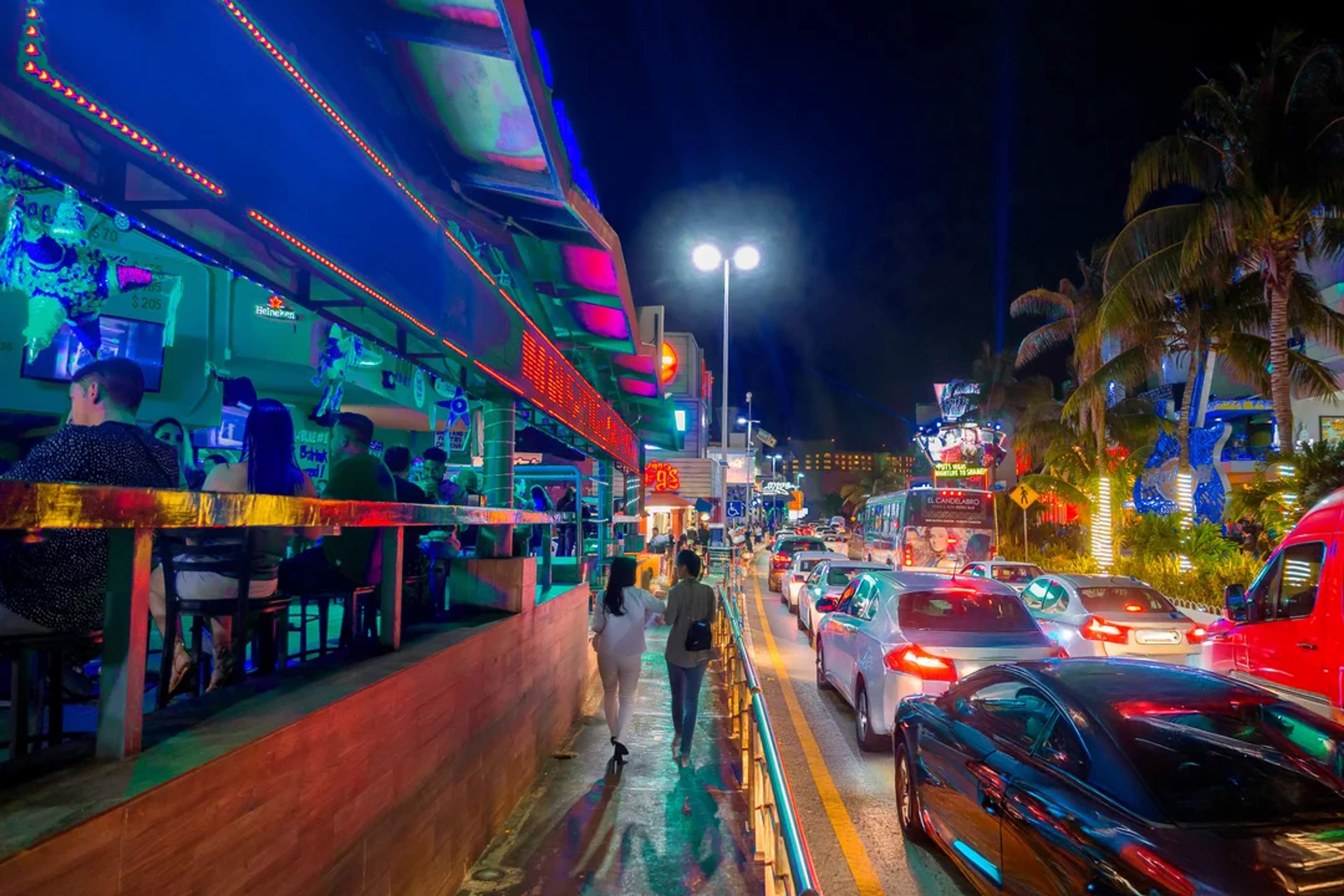 Vida nocturna vibrante en Cancún, con tráfico, luces de neón y bares llenos de energía.
