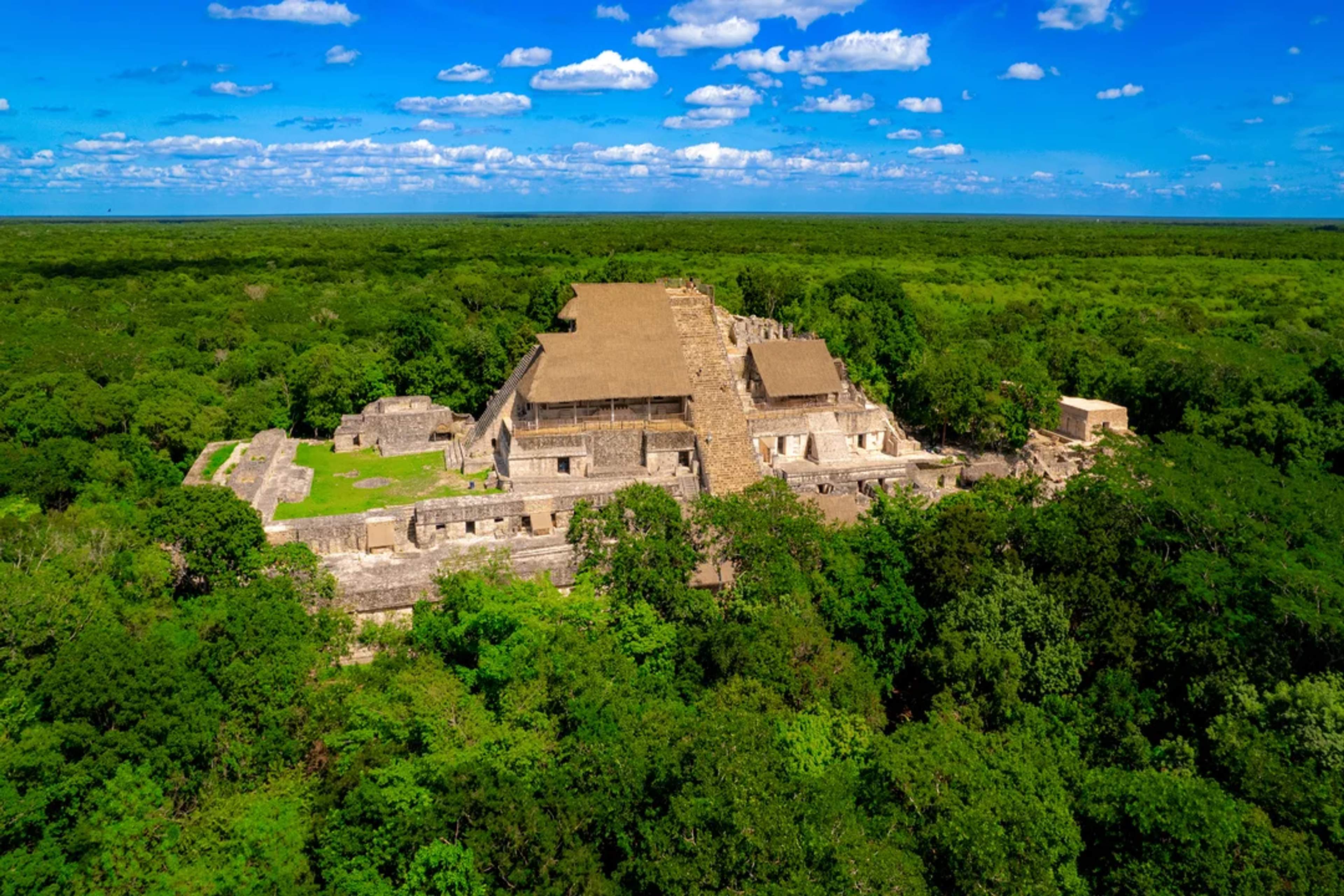 Impresionante vista aérea de un antiguo templo maya, rodeado de selva verde y bajo un cielo azul.