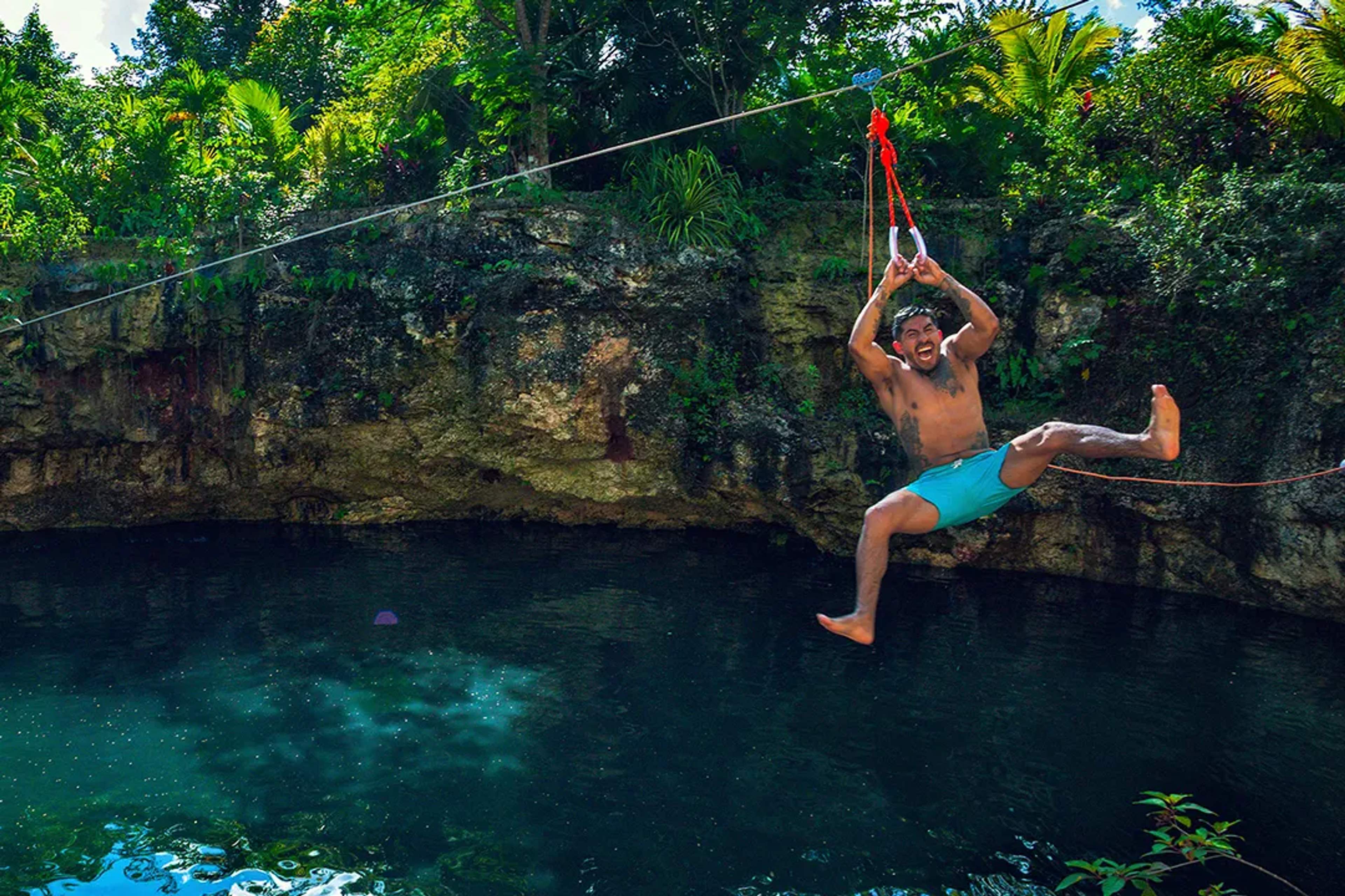 Hombre desliza en tirolesa sobre cenote en tour de aventura en Cancún rodeado de selva y agua cristalina