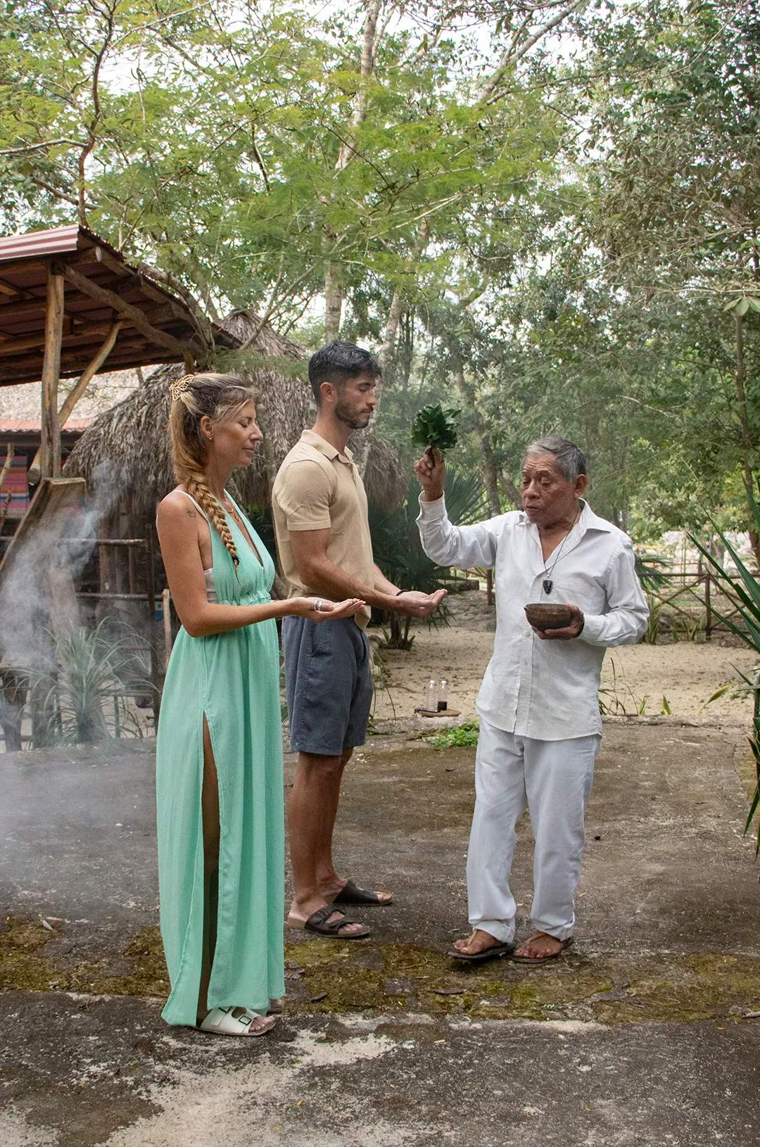 A Mayan shaman performs a purification ritual for a couple, surrounded by nature and sacred smoke.