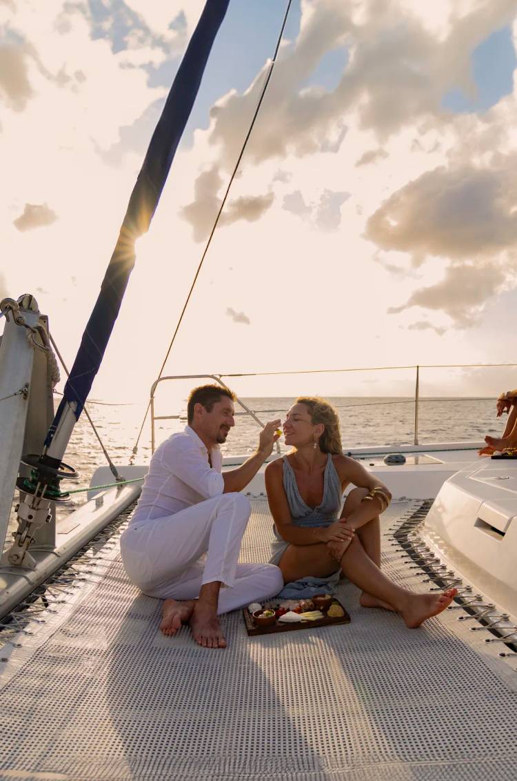 Una pareja disfruta de un momento romántico y comparte comida en un velero durante el atardecer.