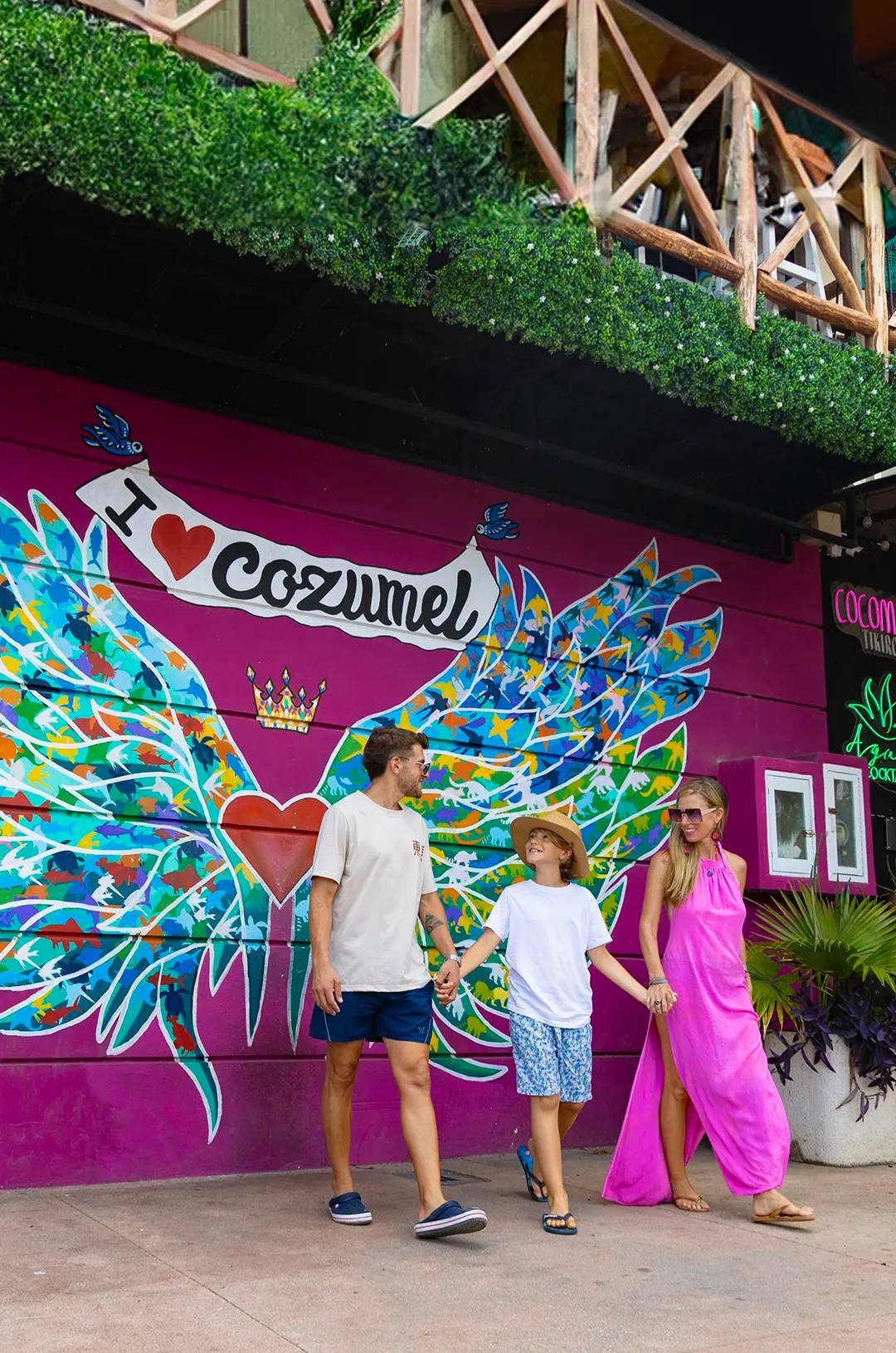 Familia caminando frente a un mural colorido que dice "I ♥ Cozumel."