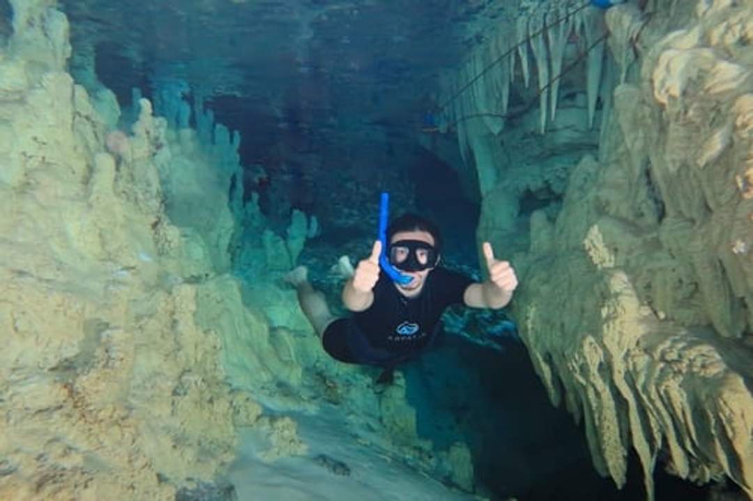 Snorkeling in a cenote in Cancun, a diver explores underwater caves with a thumbs up.