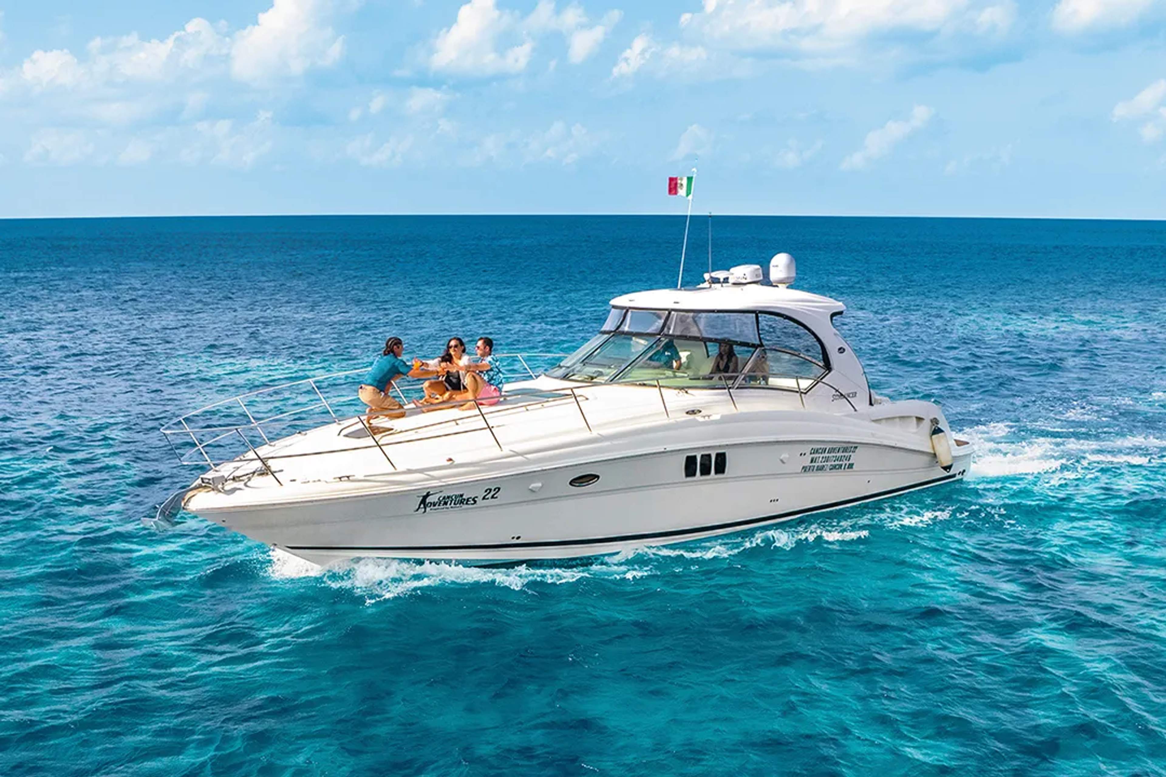 Group enjoying drinks on a luxury yacht cruising over vibrant blue waters under a sunny sky.