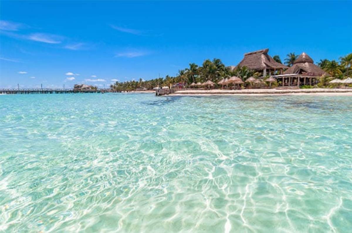 Aguas cristalinas y cabañas frente a la playa en Isla Mujeres bajo un cielo azul brillante.