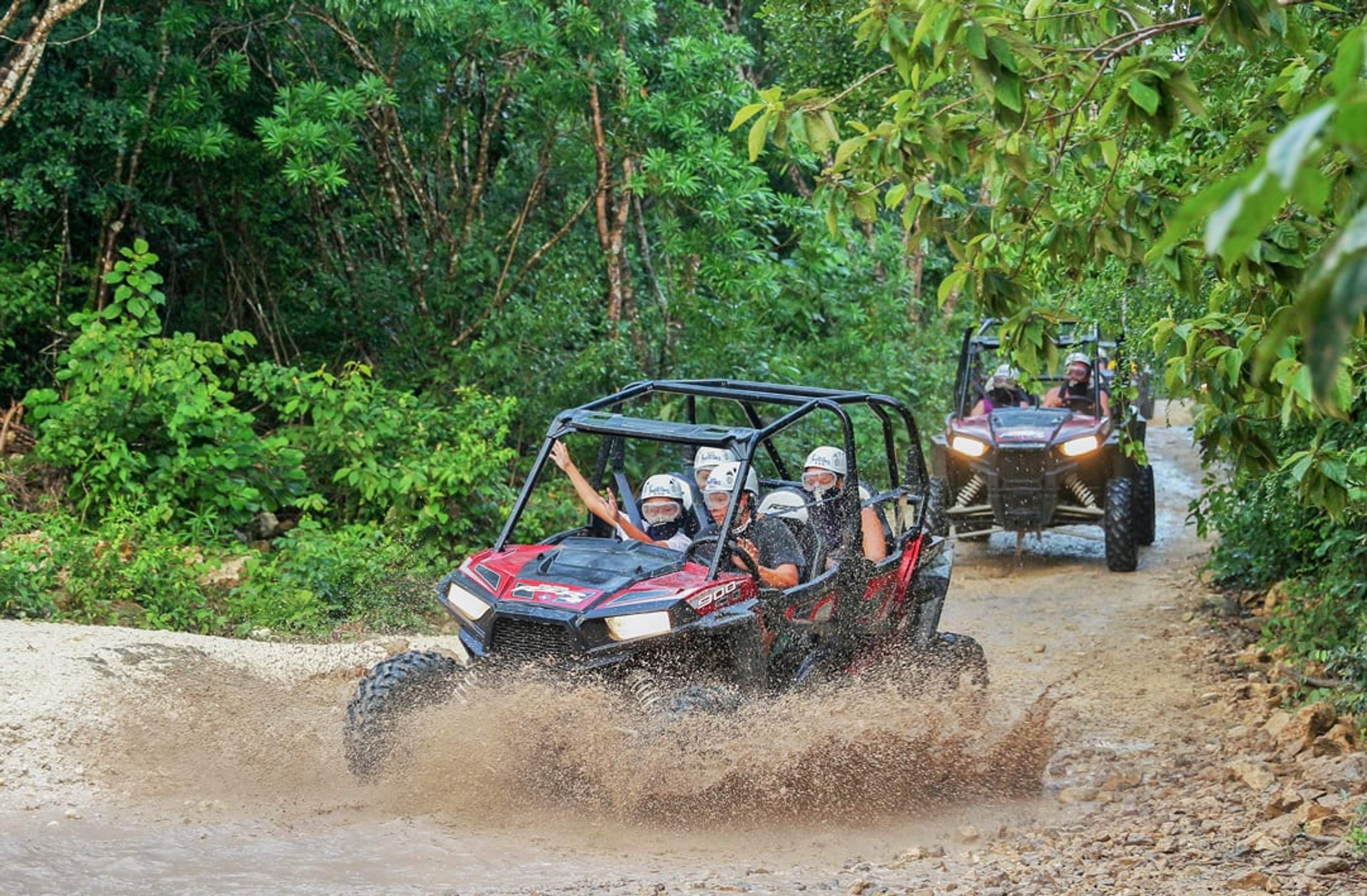 Grupo recorriendo un sendero fangoso en un vehículo todoterreno, salpicando agua, usando cascos y disfrutando la aventura.