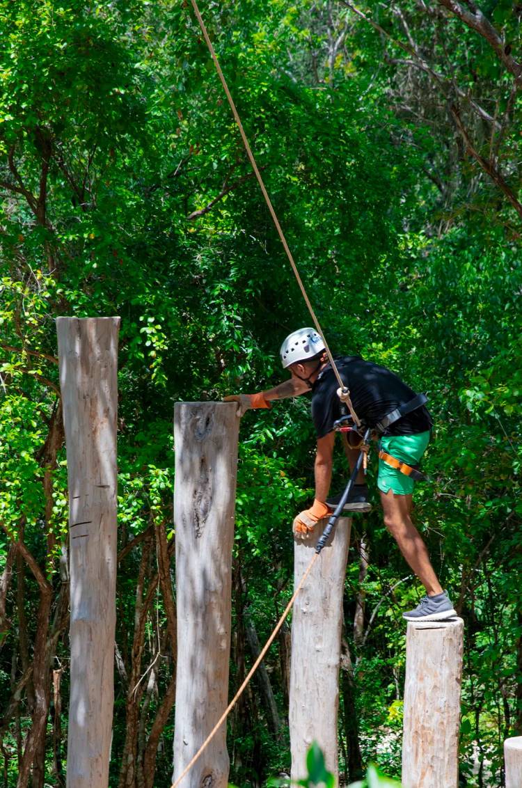 Persona en equipo de seguridad, trepando postes de madera en una aventura outdoor en Cancún.