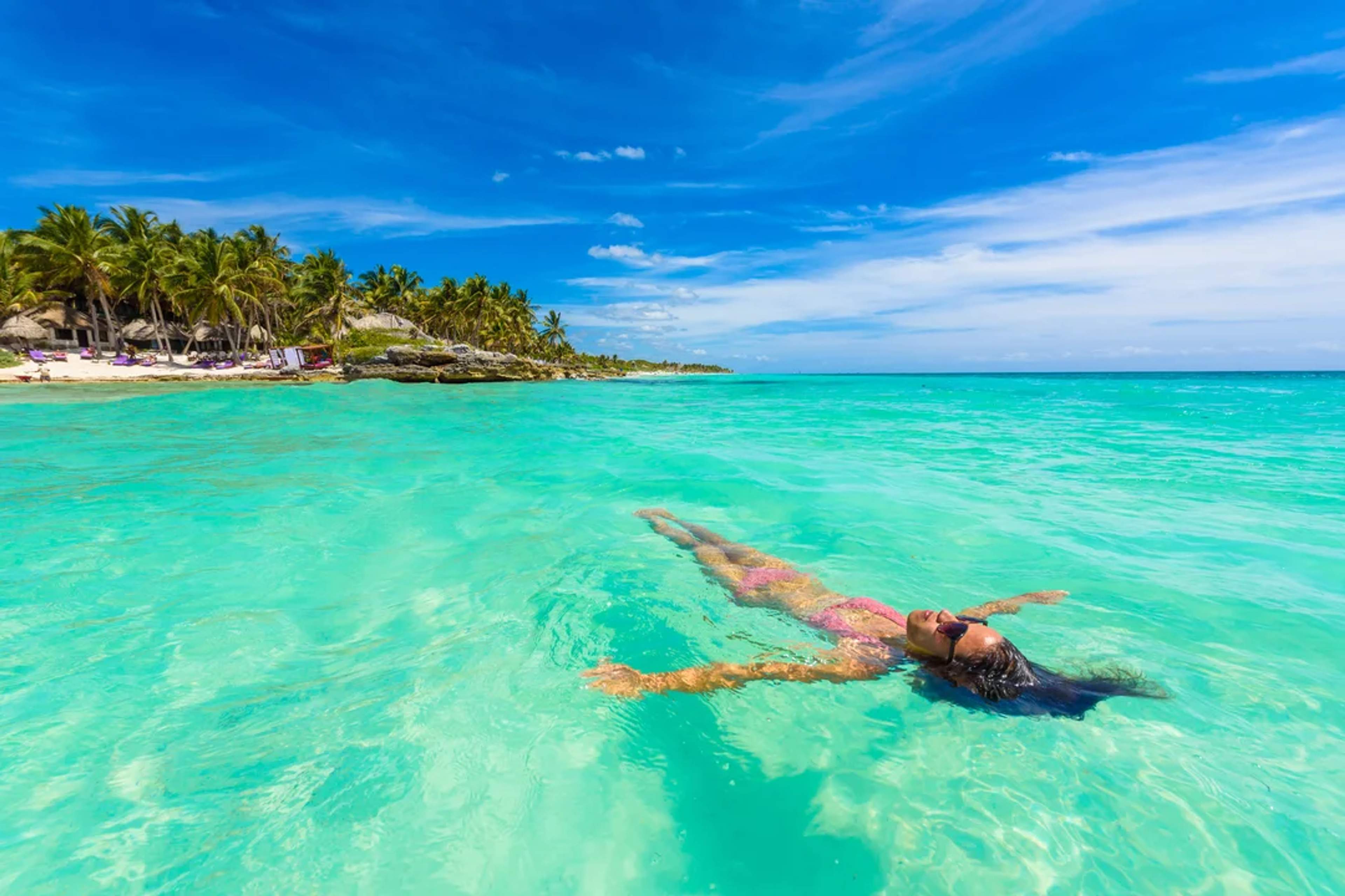 Woman floats peacefully in turquoise waters near a tropical beach under a vibrant blue sky.