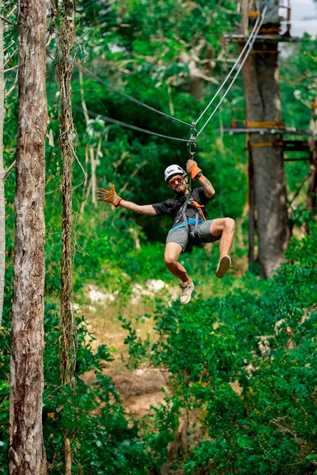 Mujer en tirolesa sobre un cenote en Cancún, salpicando agua en una emocionante aventura.