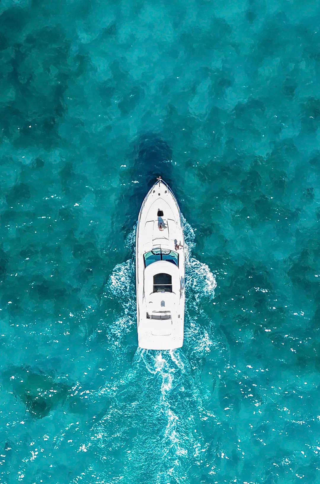 Aerial view of a yacht sailing through clear turquoise waters.