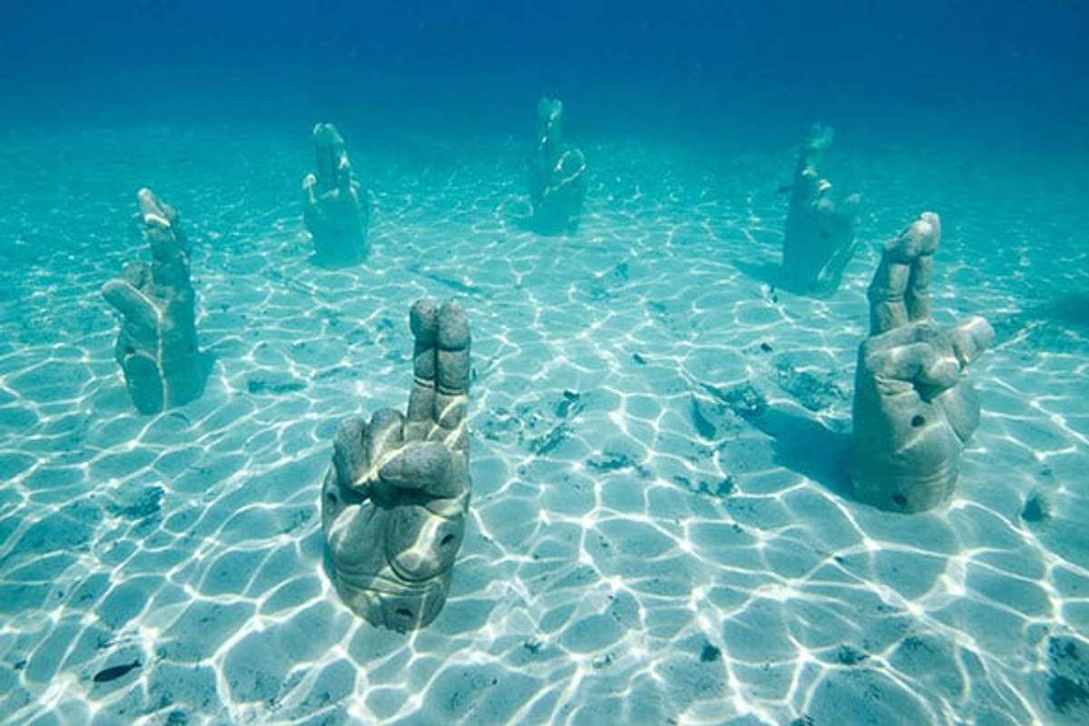 Esculturas submarinas de manos dando un gesto de bendición, ubicadas en las aguas claras y azules de Punta Sam, creando una escena etérea y serena.