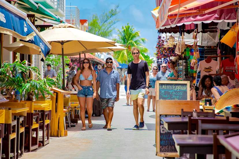 Turistas caminando por un colorido mercado callejero en Cancún, México, disfrutando comida y compras.