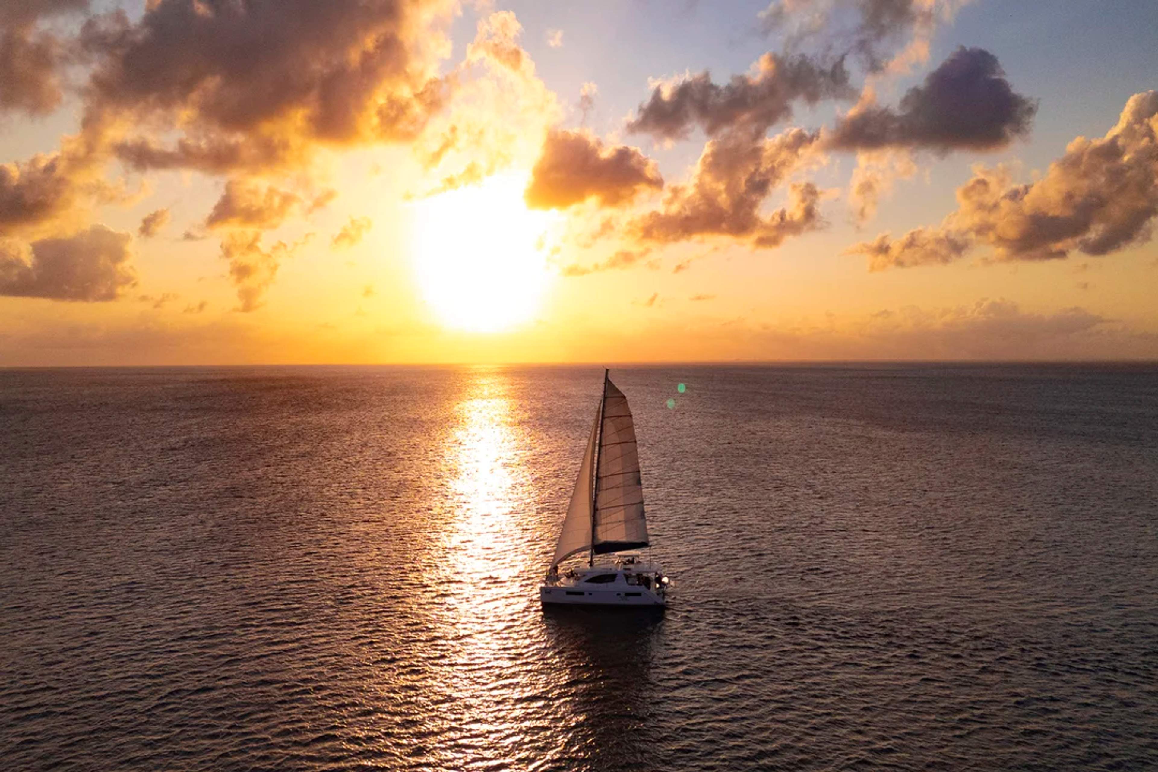 Catamaran sails into a golden sunset over calm ocean waters, creating a dreamy seascape.