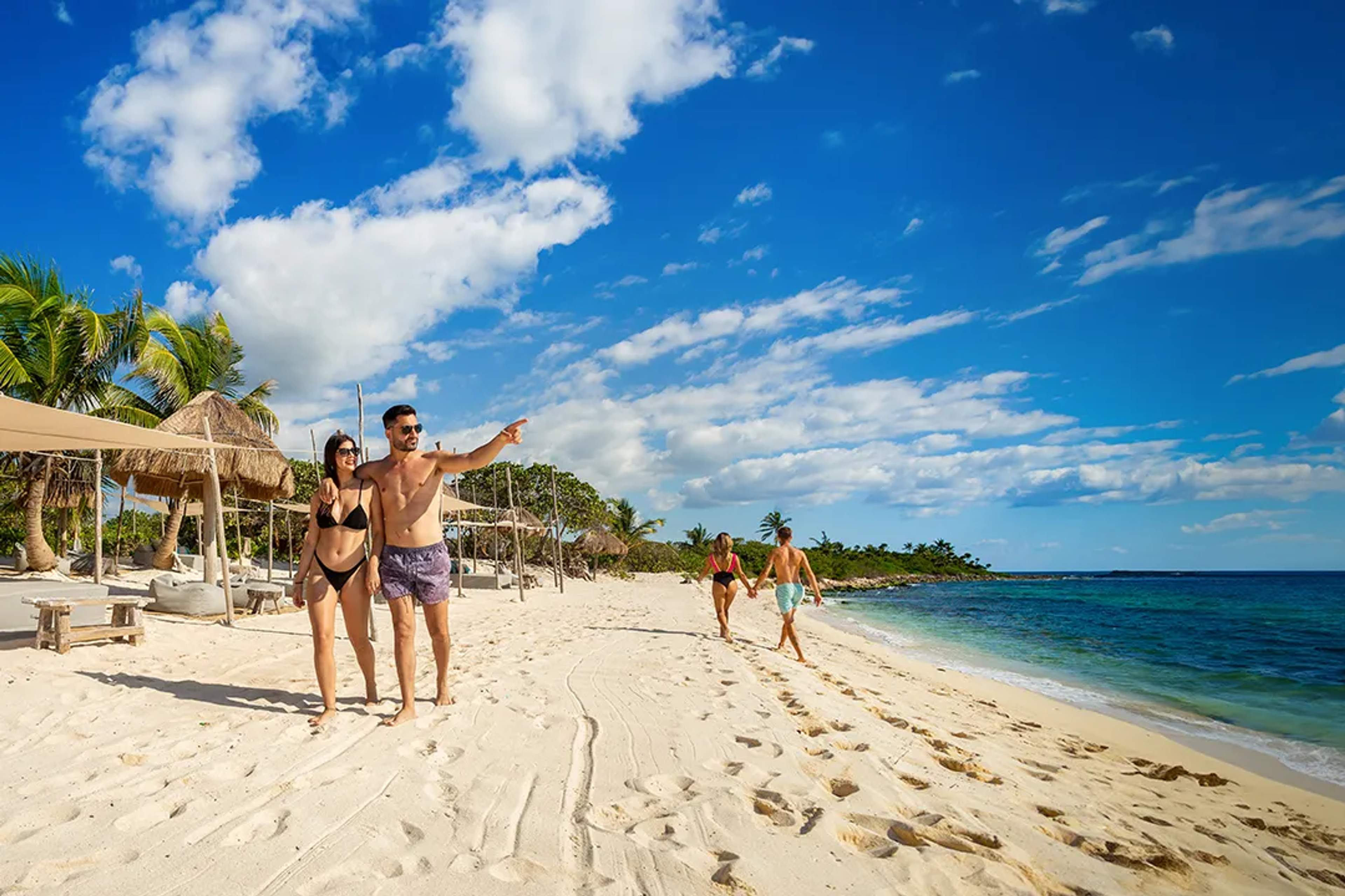 Parejas disfrutando de un día soleado en una playa prístina de Cancún, un destino ideal para vivir.