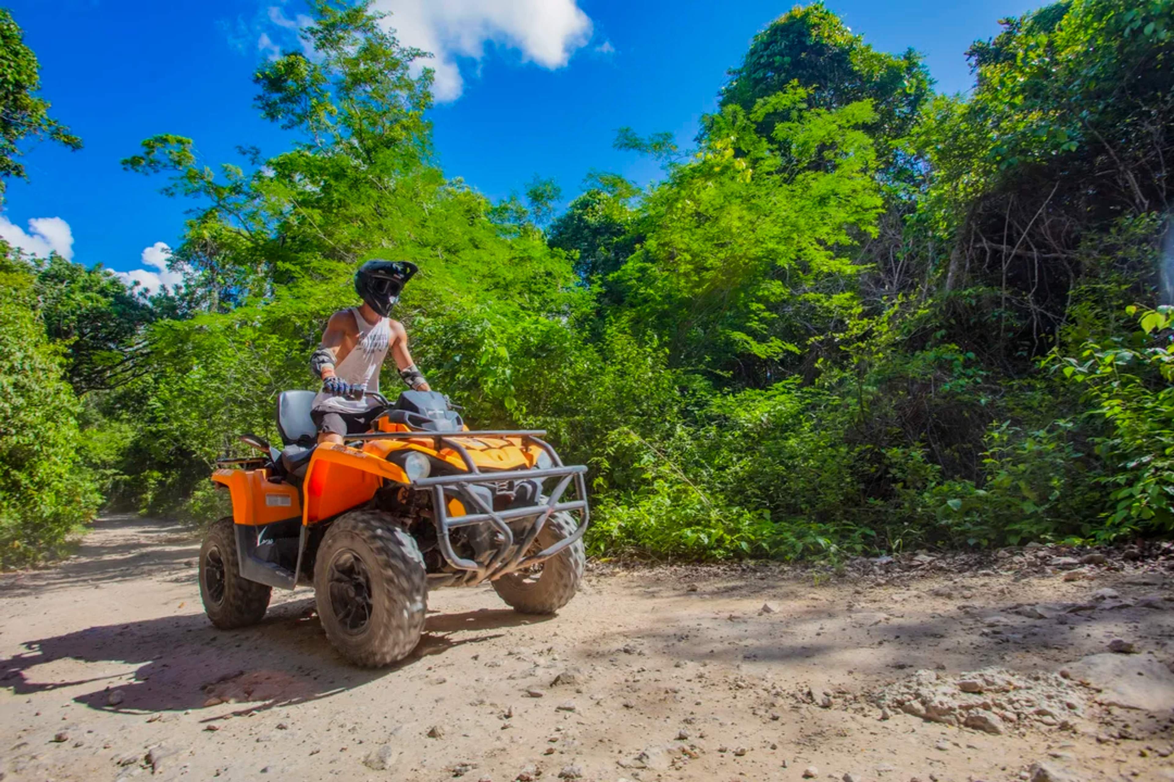 Turista maneja un ATV por un sendero selvático bajo el sol en una aventura extrema en Cancún.