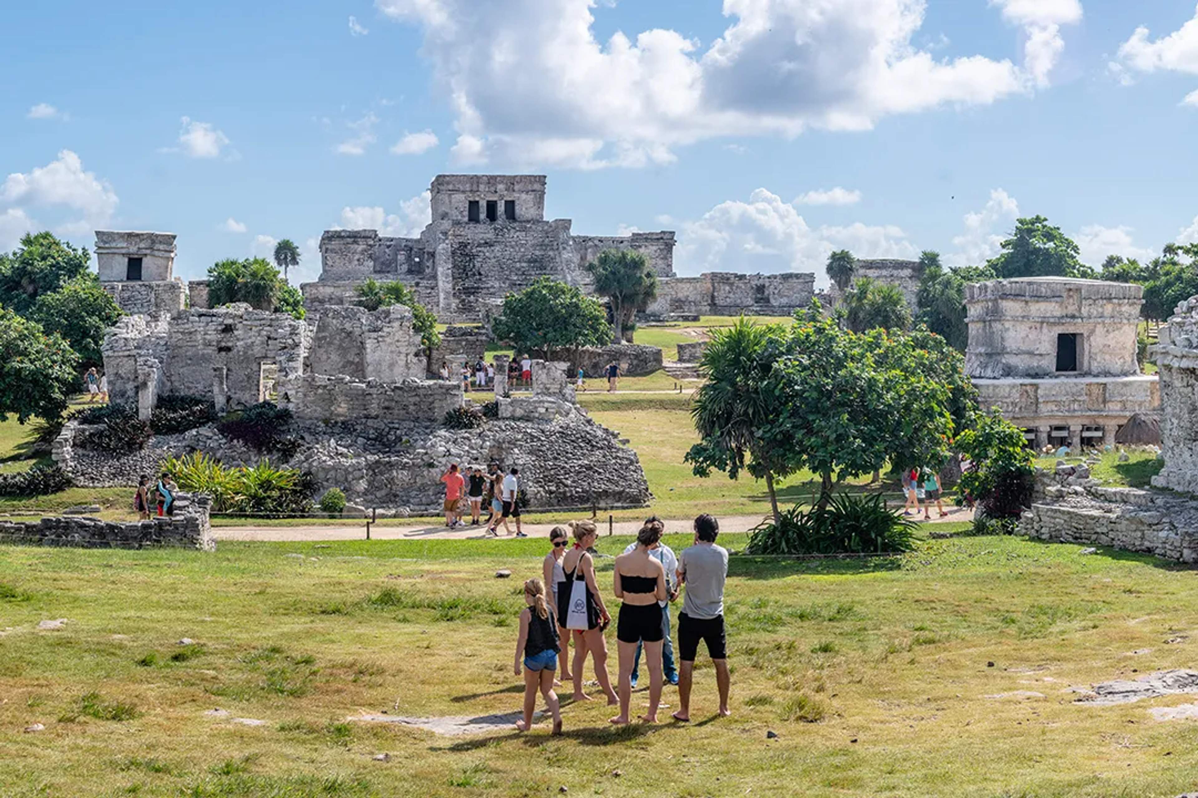 Visitors exploring the Tulum Mayan ruins with stone temples, ocean views, and lush greenery in Cancun