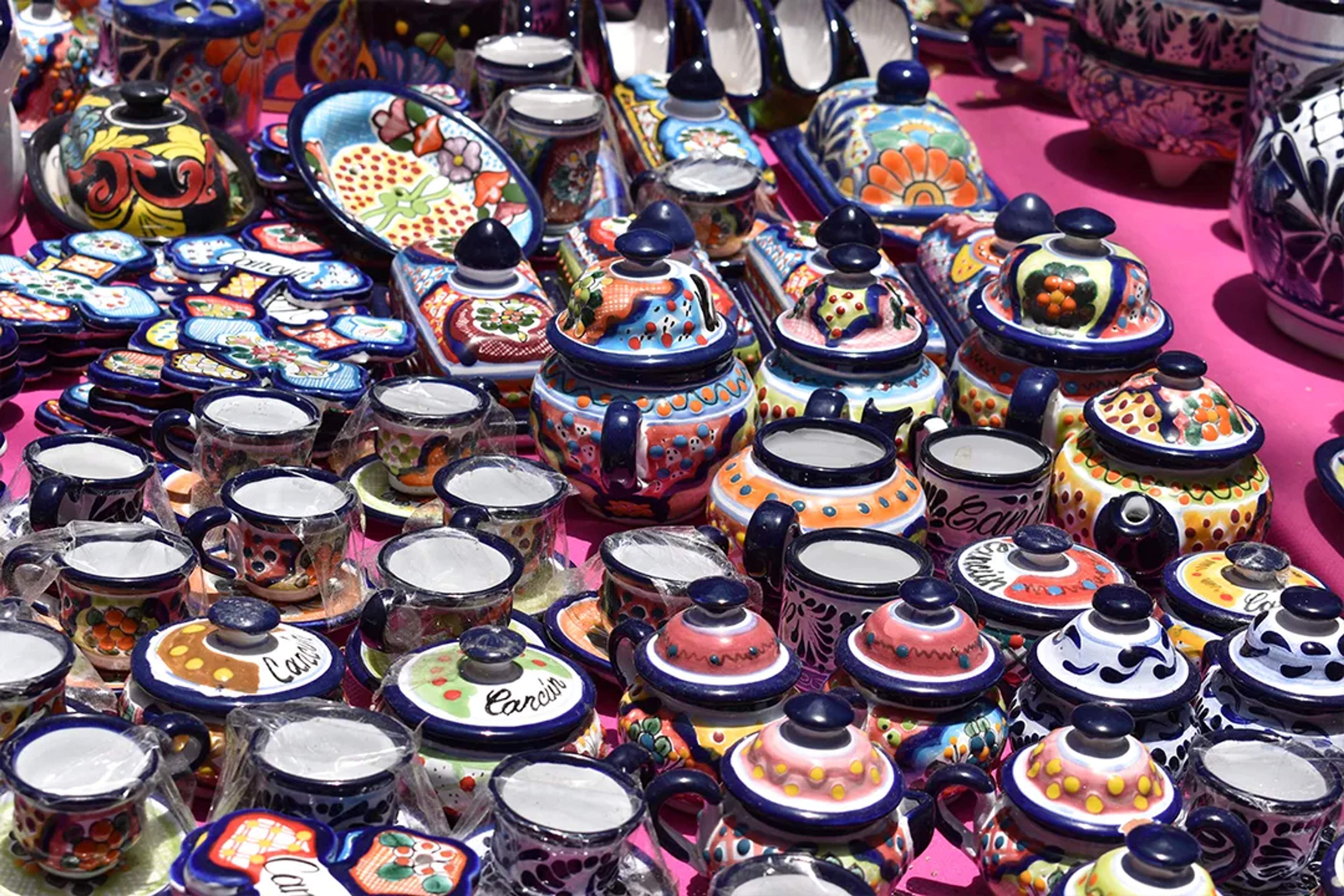 Colorida talavera mexicana en un mercado, con tazas, tapas y piezas decorativas.