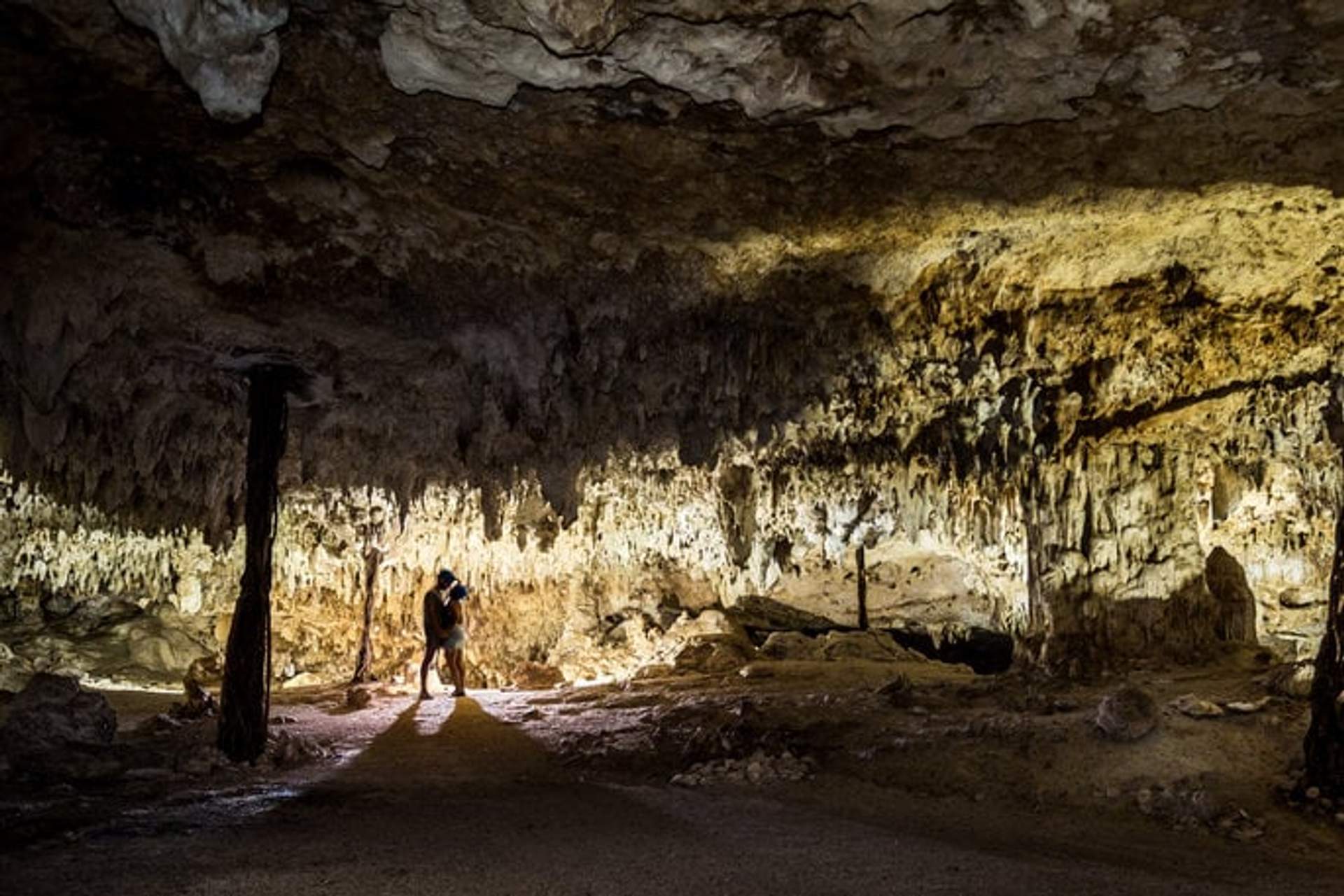 A couple standing and embracing in a dimly lit cave with stunning stalactites and rock formations in Tulum.