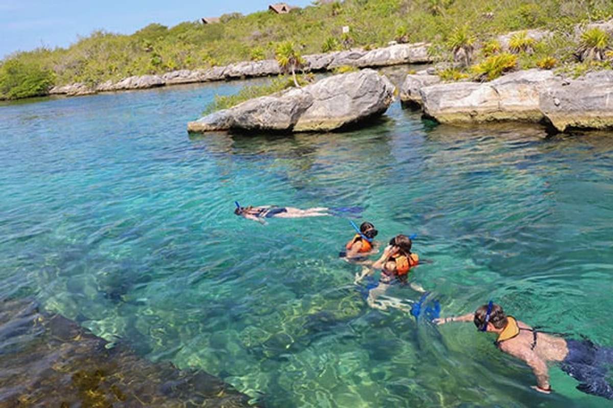 Personas haciendo snorkel en las aguas claras y turquesas de la Laguna Yal-kú en Playa del Carmen, rodeadas de costas rocosas y vegetación.