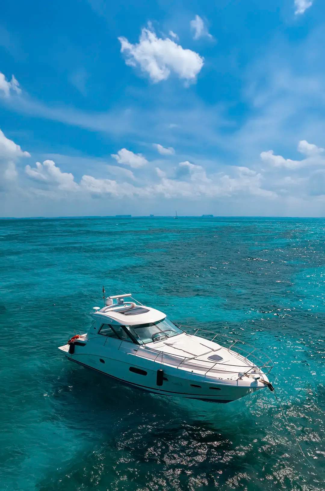 A white yacht anchored in clear turquoise waters on a sunny day, with distant ships on the horizon.