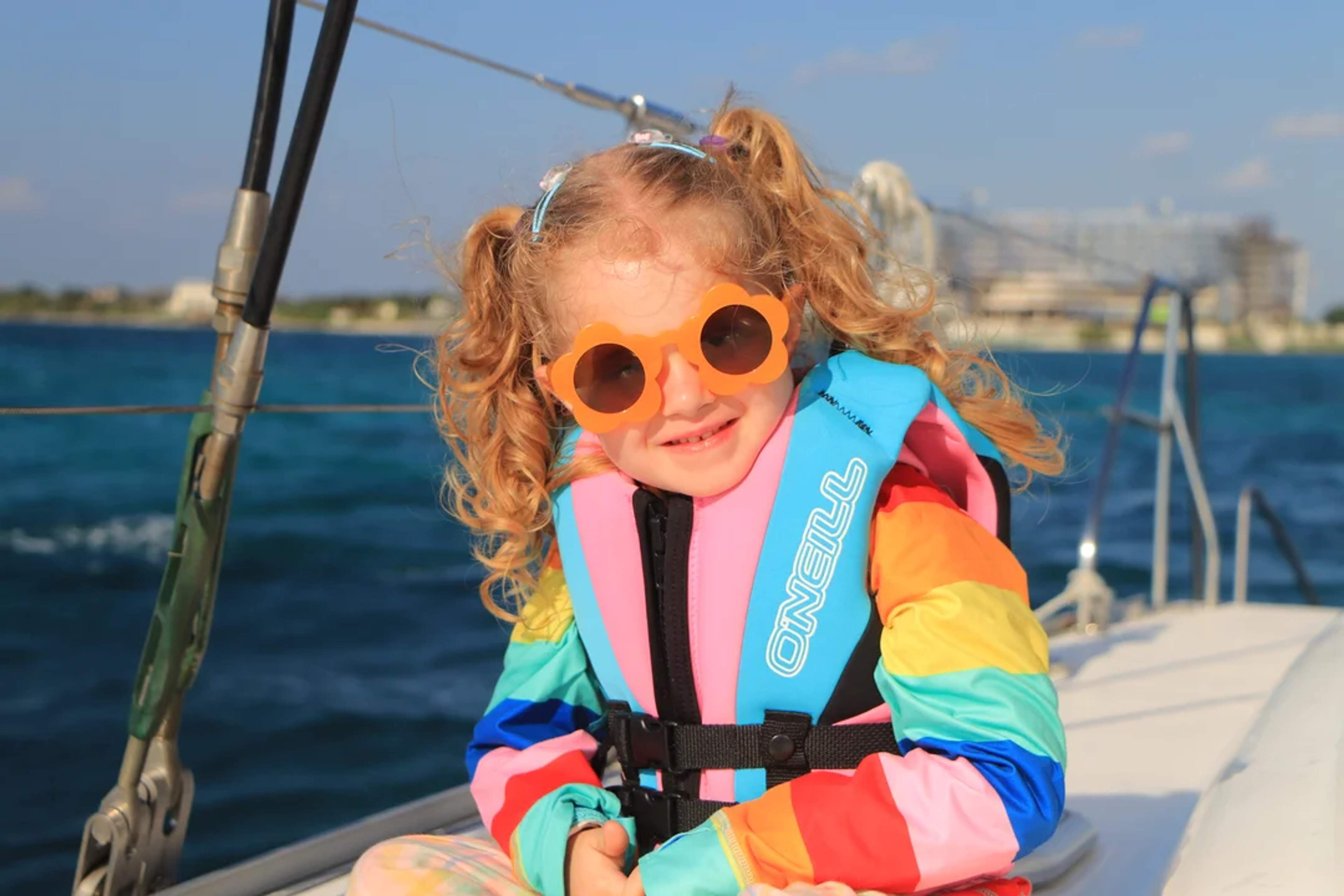 Niña con lentes divertidos y chaleco salvavidas disfruta un paseo en barco bajo el sol.