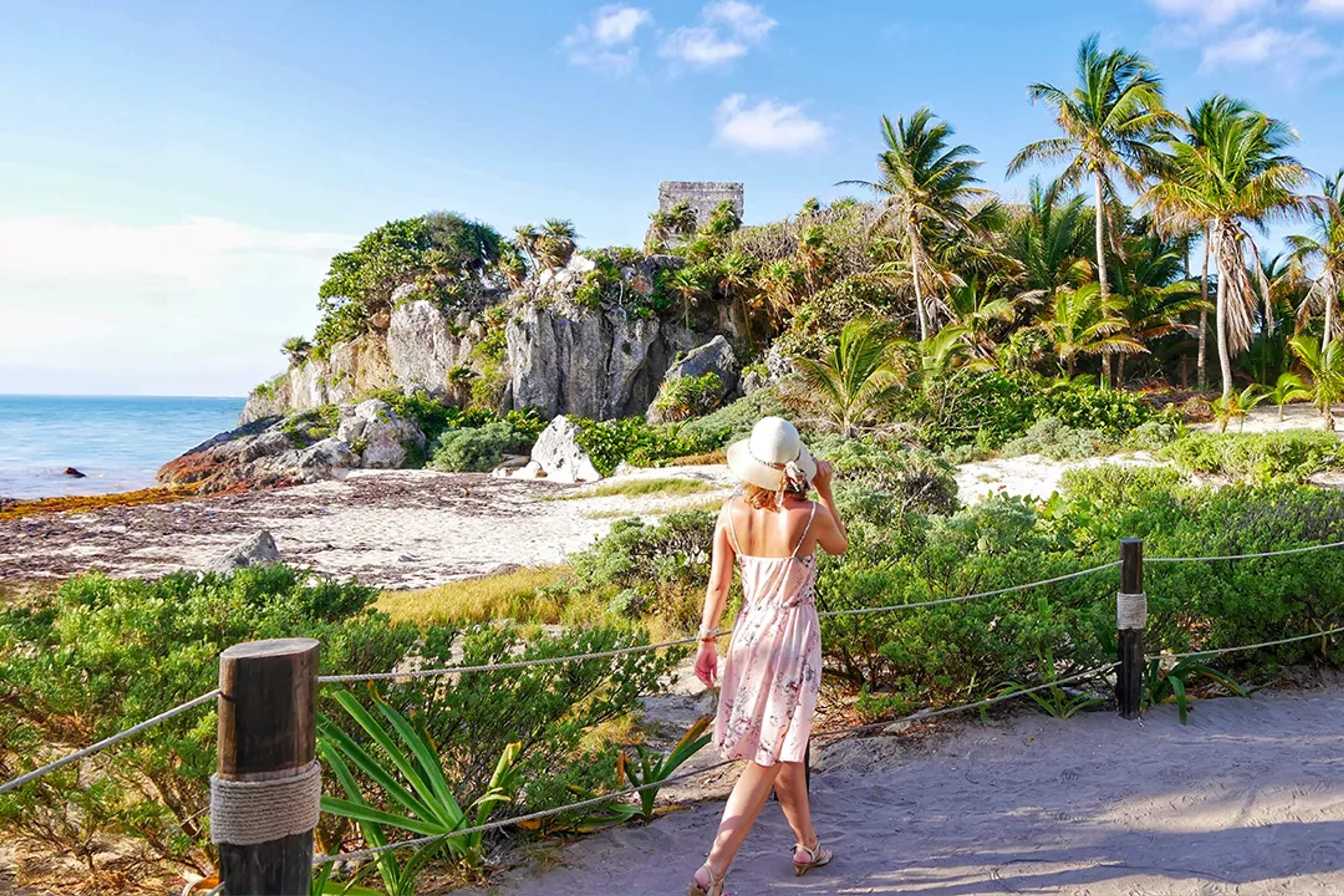 Woman in summer dress admiring Tulum ruins by the beach.