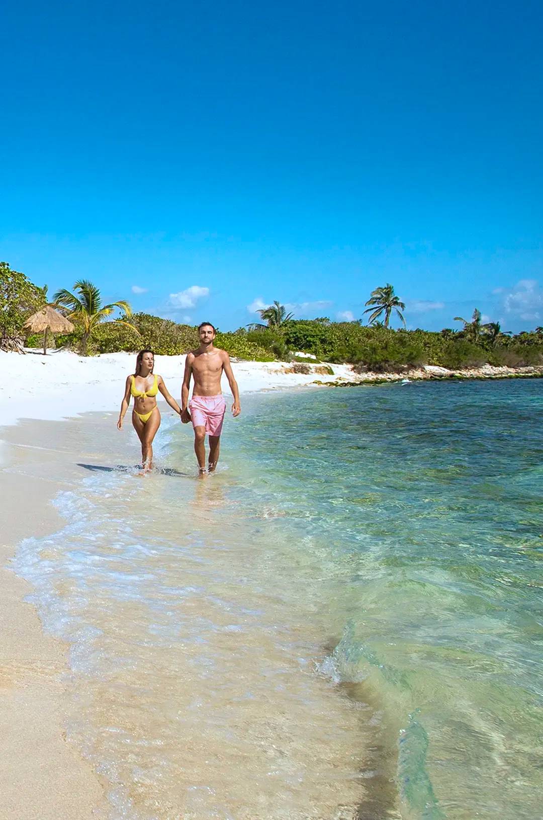 A couple walking hand in hand along a sandy beach in Cancun.