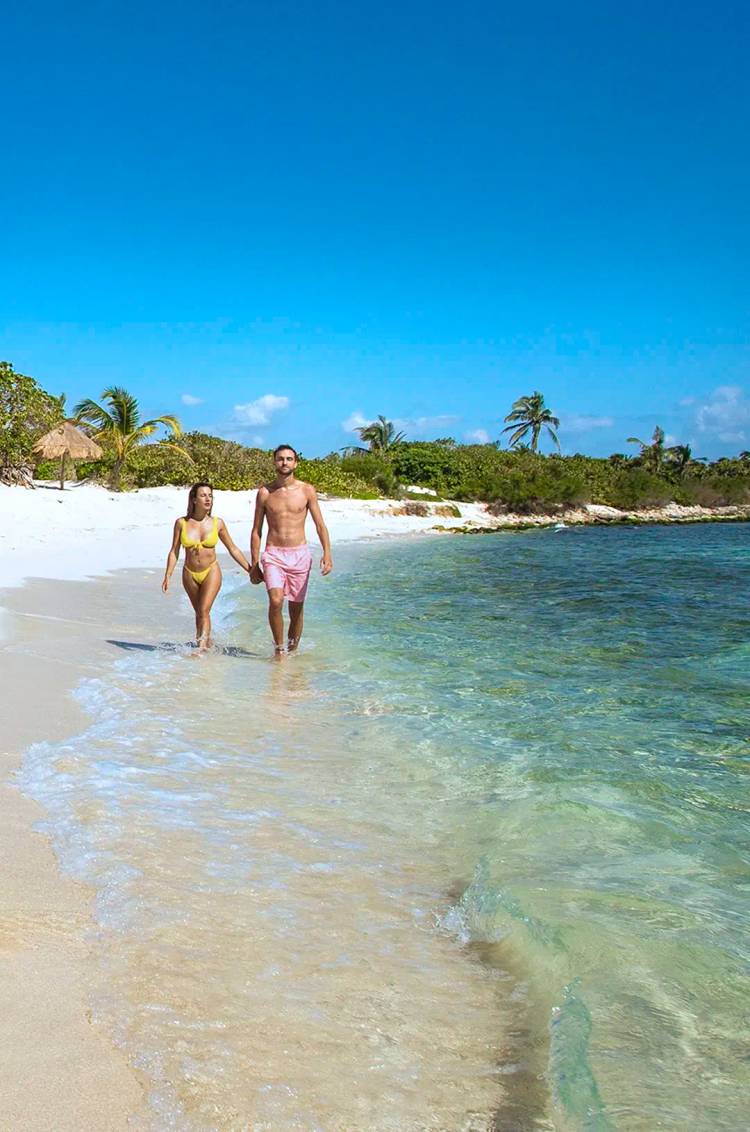 A couple walking hand in hand along a sandy beach in Cancun.