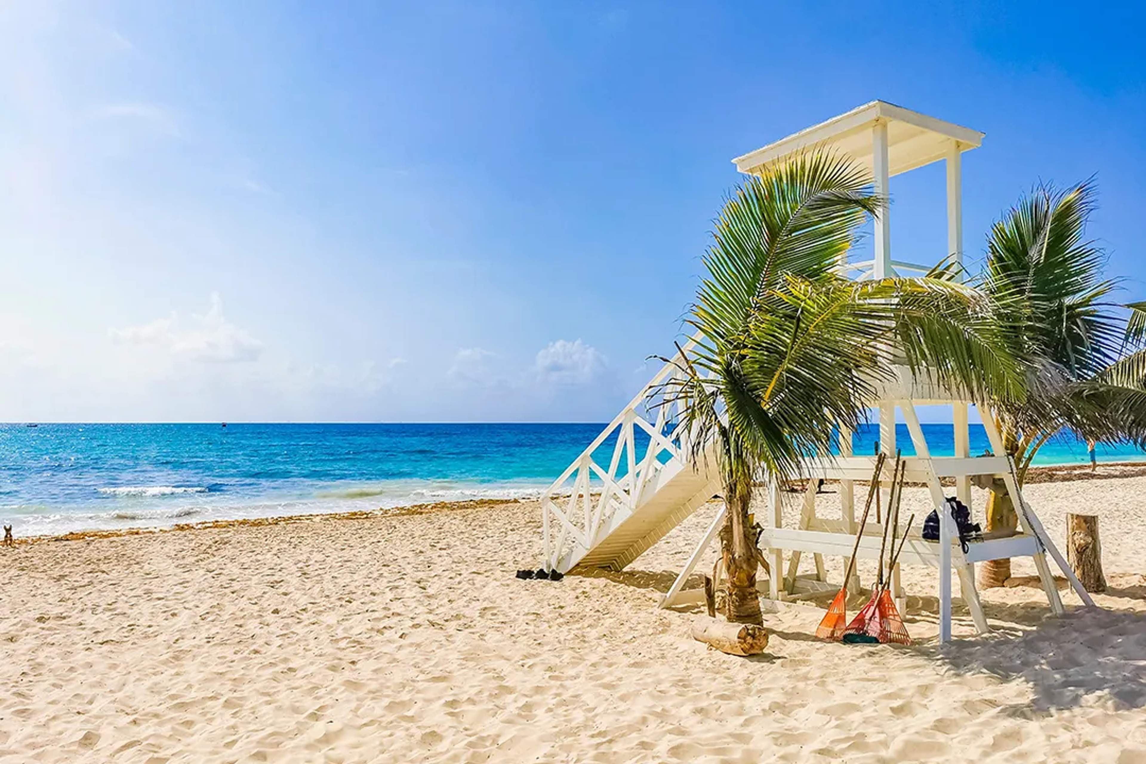 Torre de salvavidas blanca en playa de Cancun con palmeras, mar Caribe turquesa y cielo azul despejado