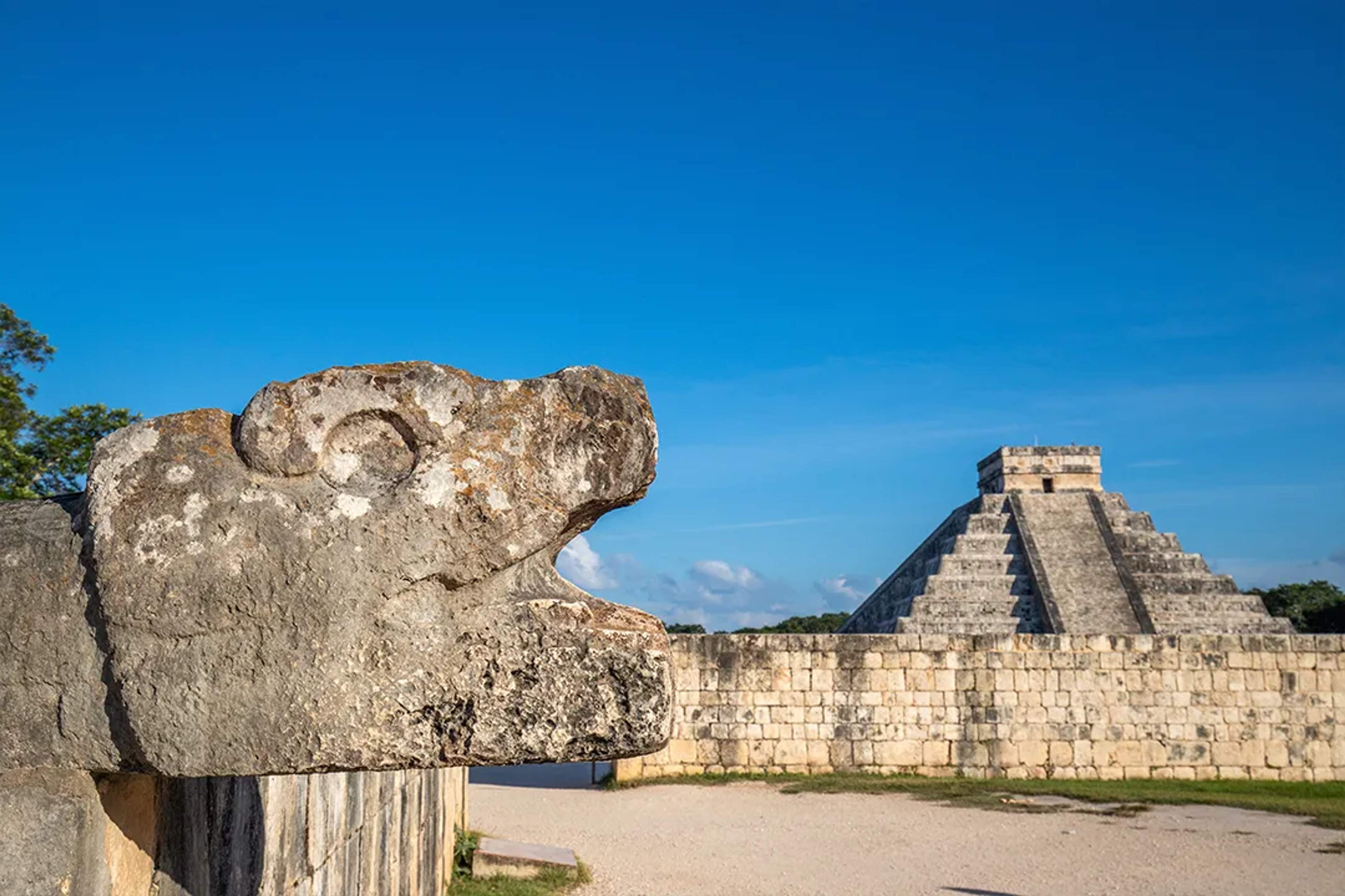 Chichen Itza pyramid and stone serpent sculpture under a clear blue sky in the Yucatán Peninsula.