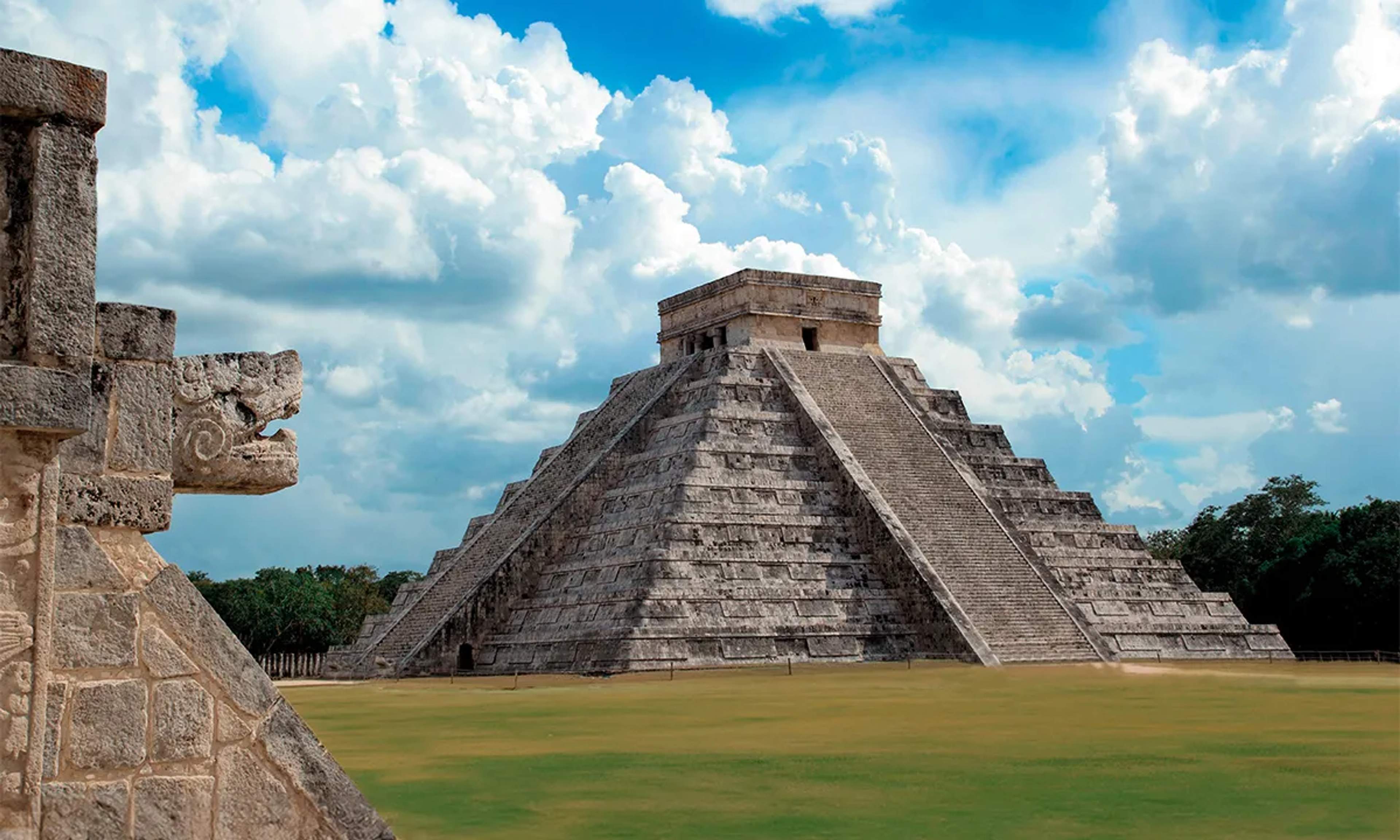 Vista de la pirámide de Kukulkán en Chichén Itzá, con una escultura de serpiente en primer plano.ón densa.
